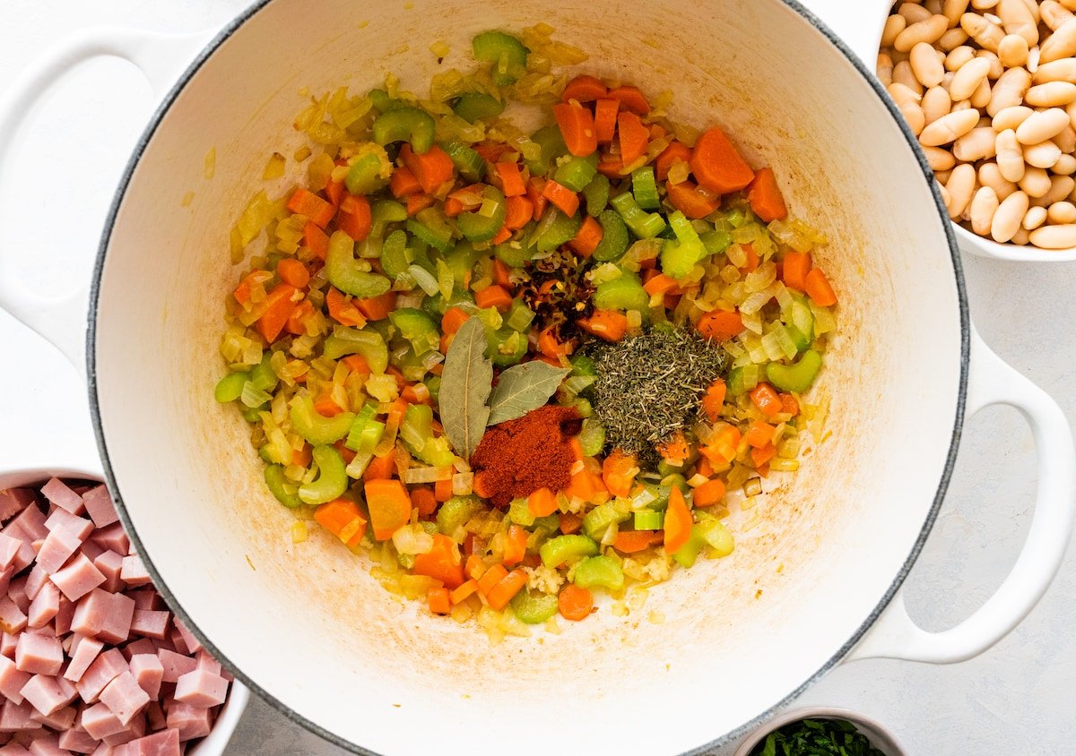 vegetables with herbs and spices cooking in large pot to make ham and bean soup. 