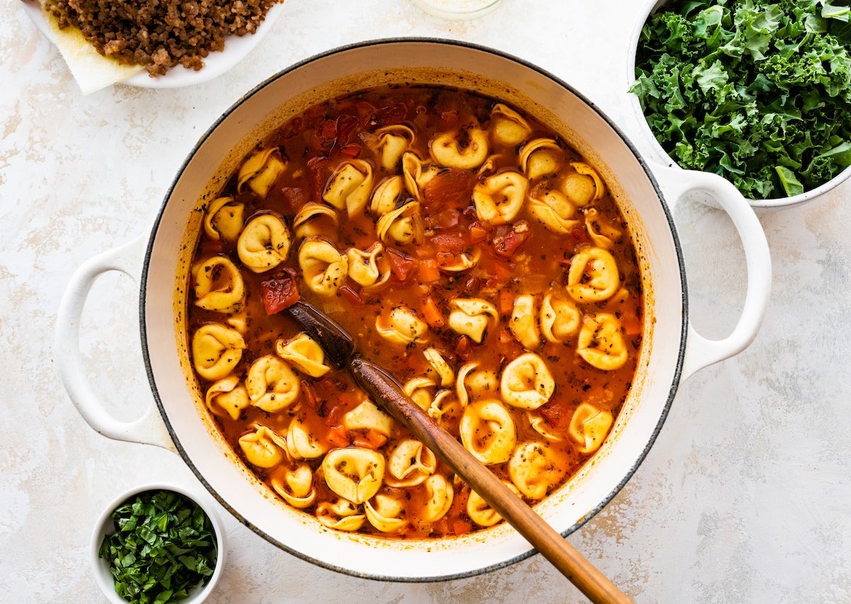 Italian sausage tortellini soup in pot with wooden spoon. 