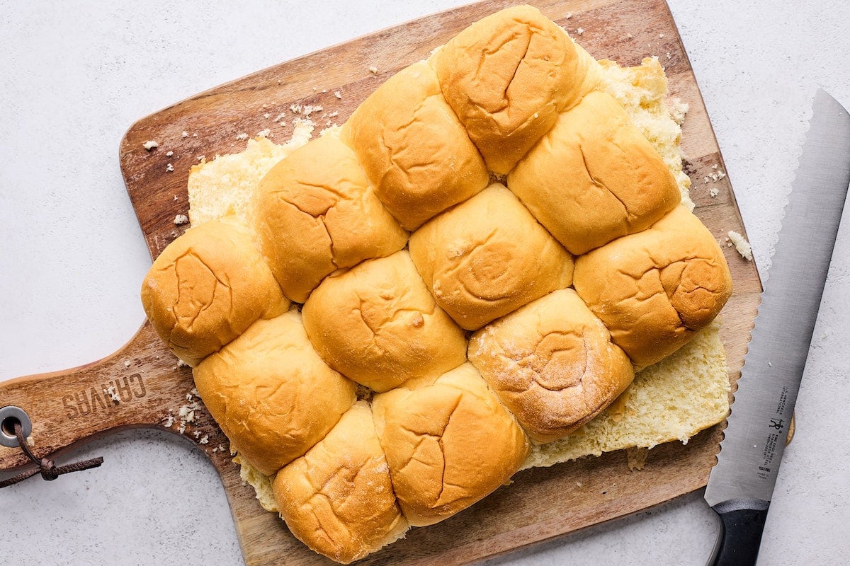 Hawaiian sweet rolls being cut in half with sharp bread knife. 