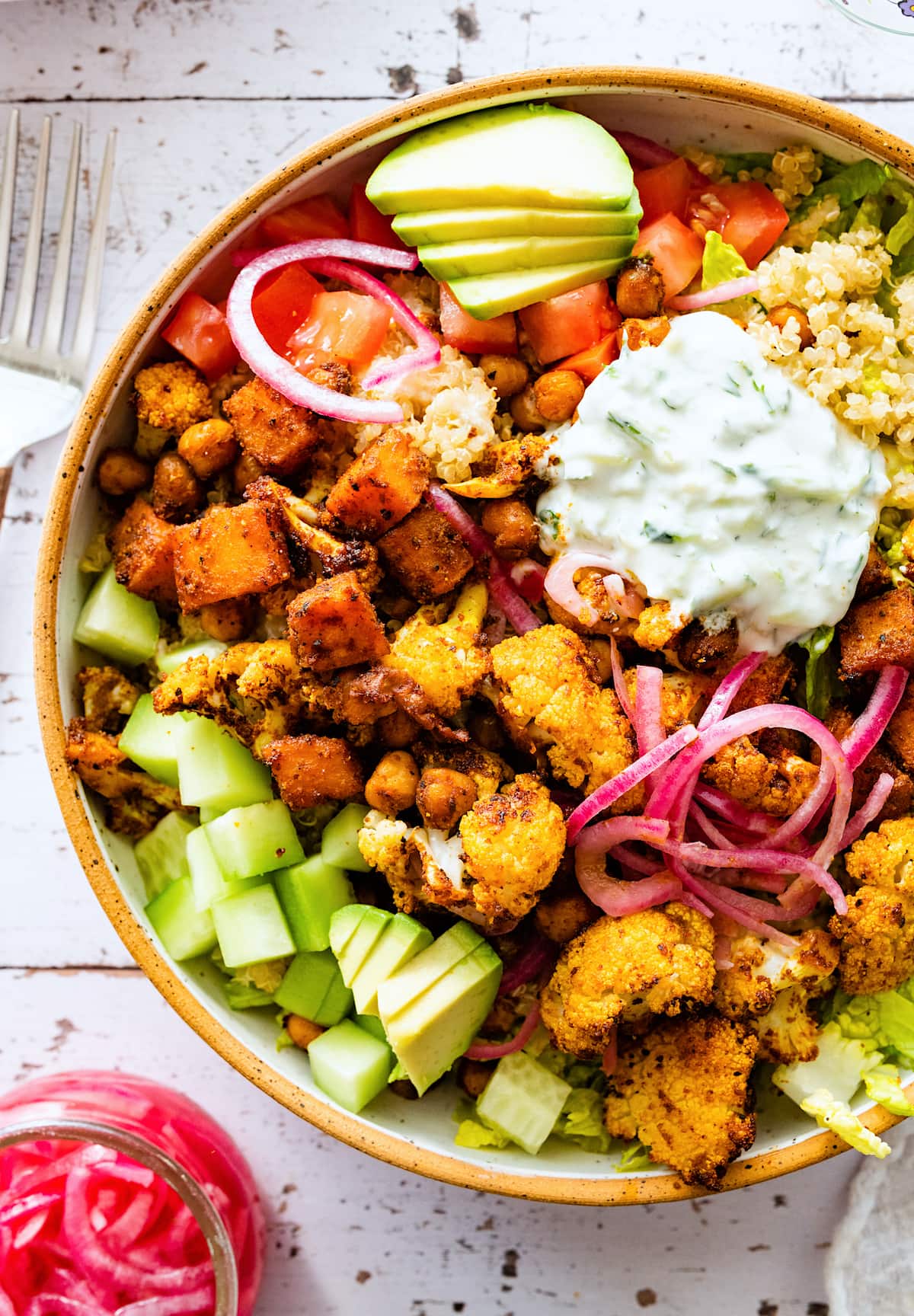 roasted cauliflower sweet potato chickpea bowl with tzatziki and toppings.