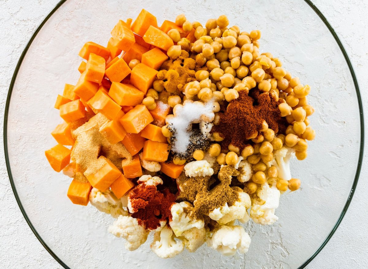 cauliflower, sweet potatoes, chickpeas, and spices in mixing bowl. 