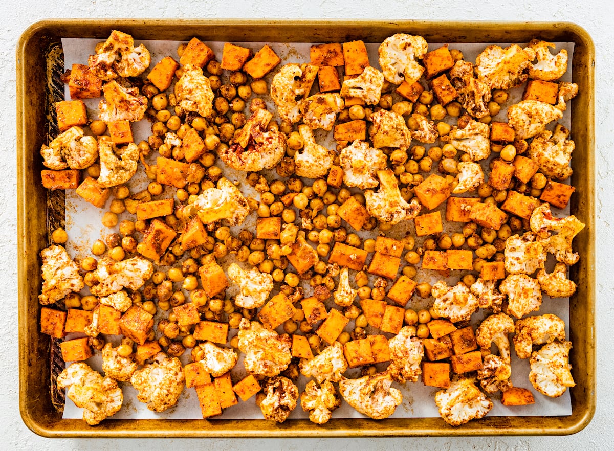 cauliflower, sweet potatoes, chickpeas, and spices on baking sheet. 