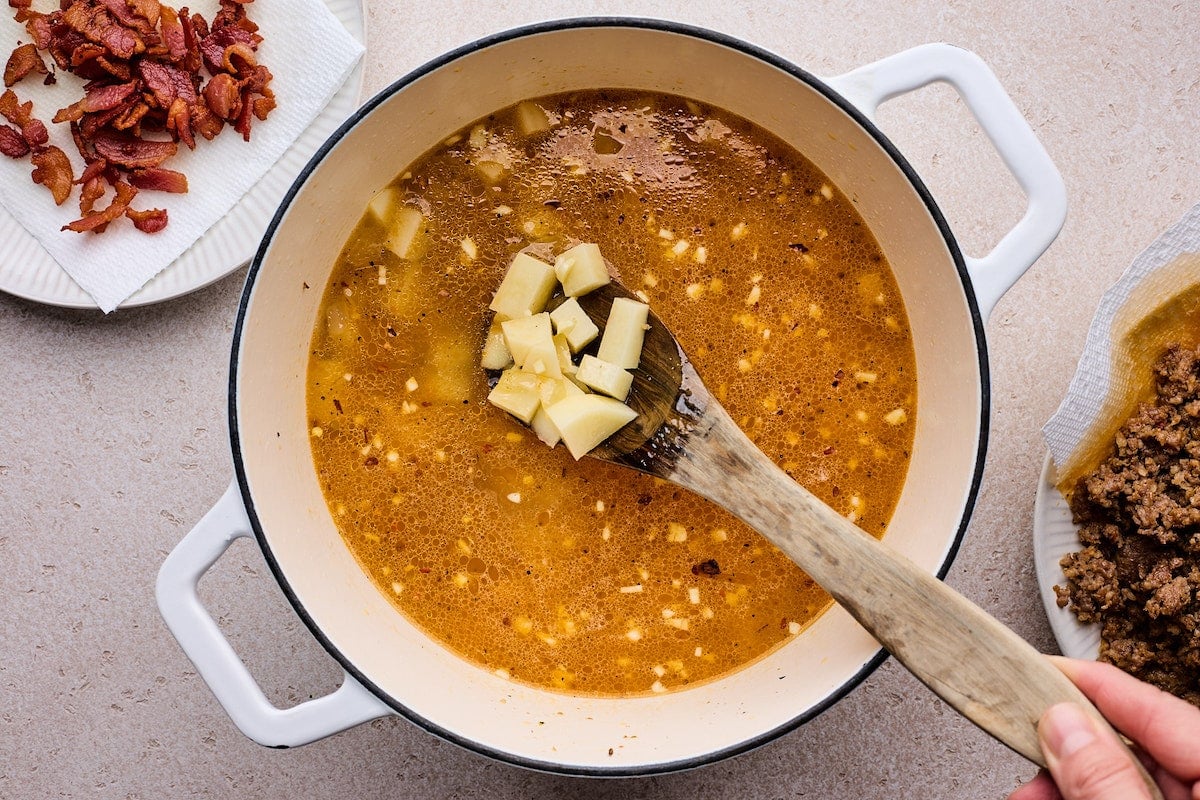 potatoes cooking in broth in large white pot to make zuppa toscana. 