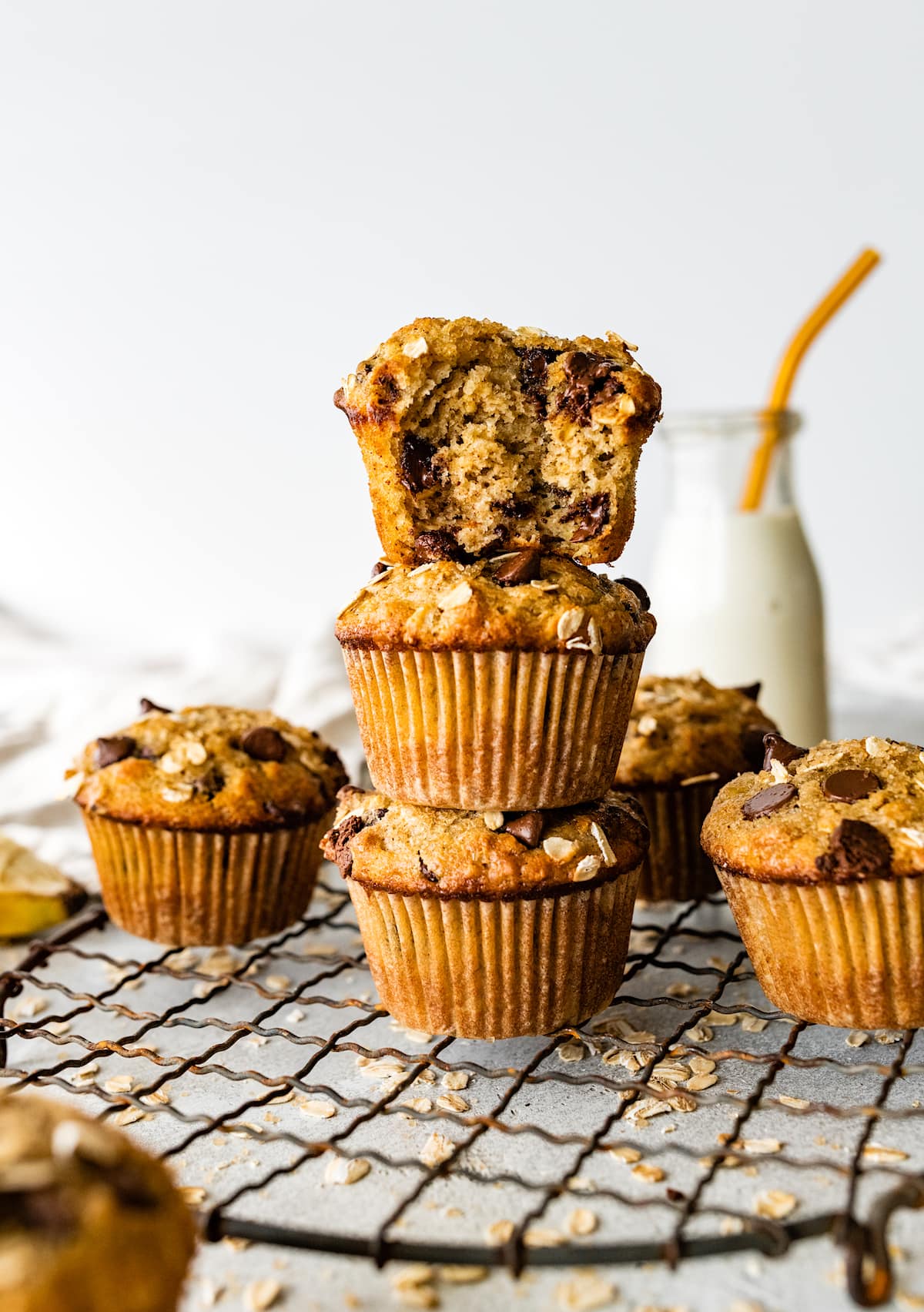 stack of banana oatmeal muffins with chocolate chips on cooling rack with bottle of milk. 
