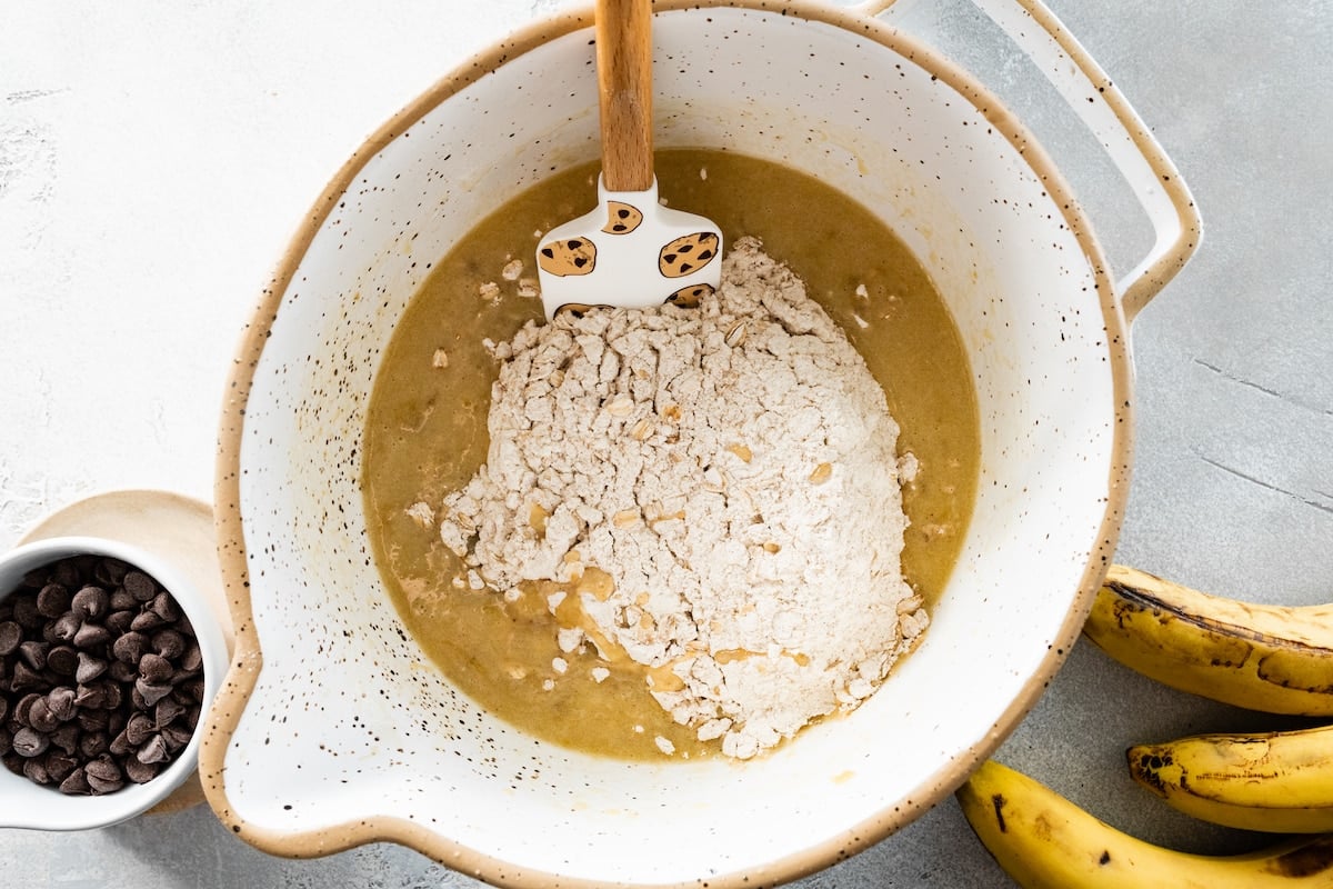 adding dry ingredients to wet ingredients in mixing bowl to make banana oatmeal muffins. 