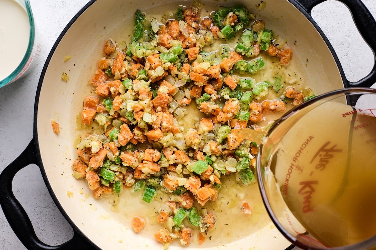 chicken broth being poured into skillet with onion, carrots, celery, and flour. 