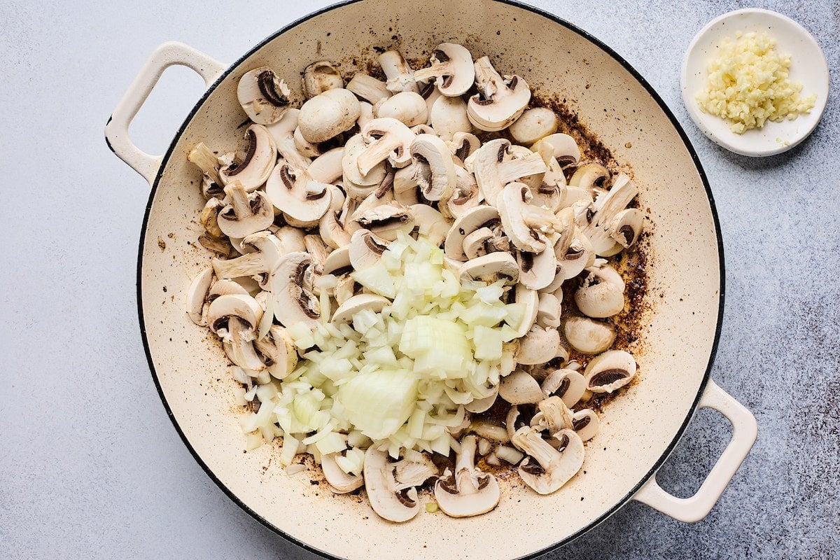 mushrooms and onion cooking in skillet to make beef stroganoff.