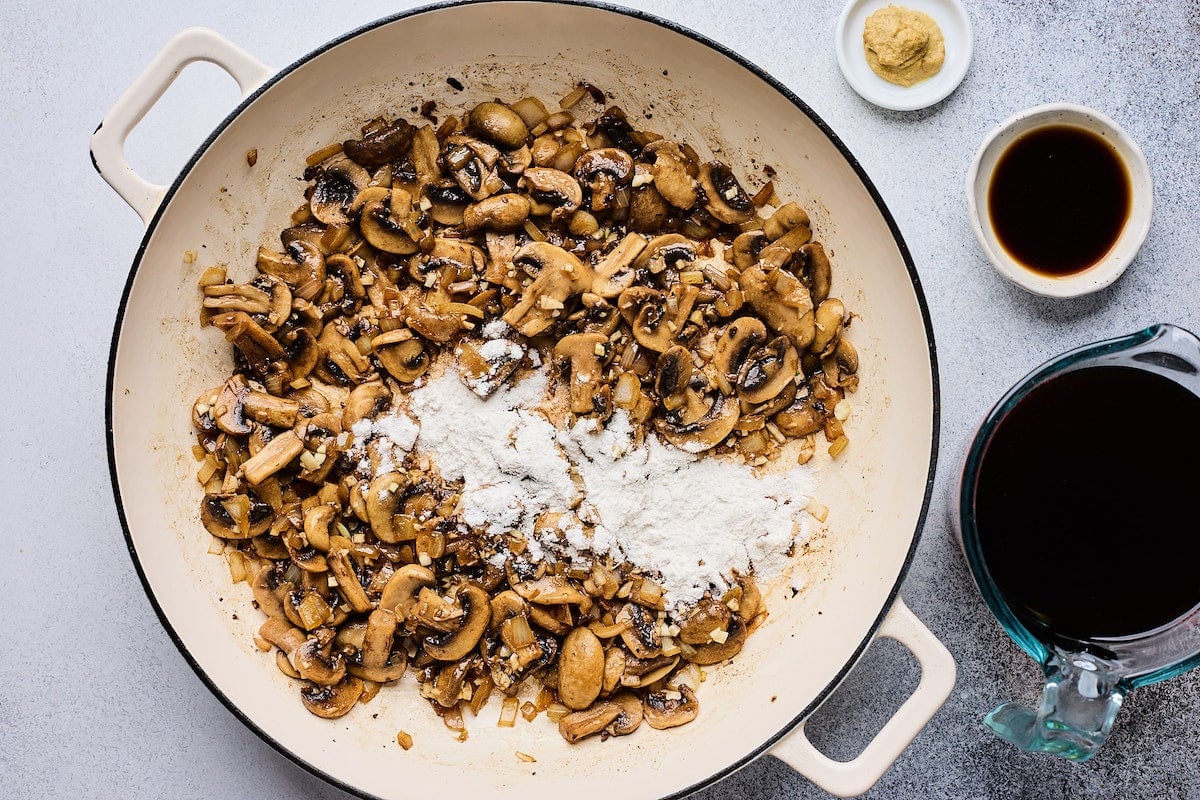 flour being added to mushrooms in skillet.