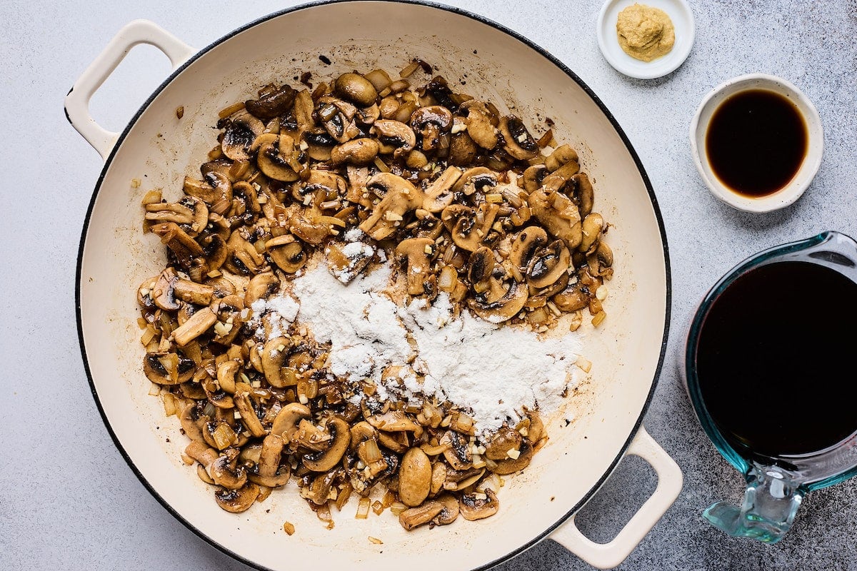 flour being added to mushrooms in skillet. 