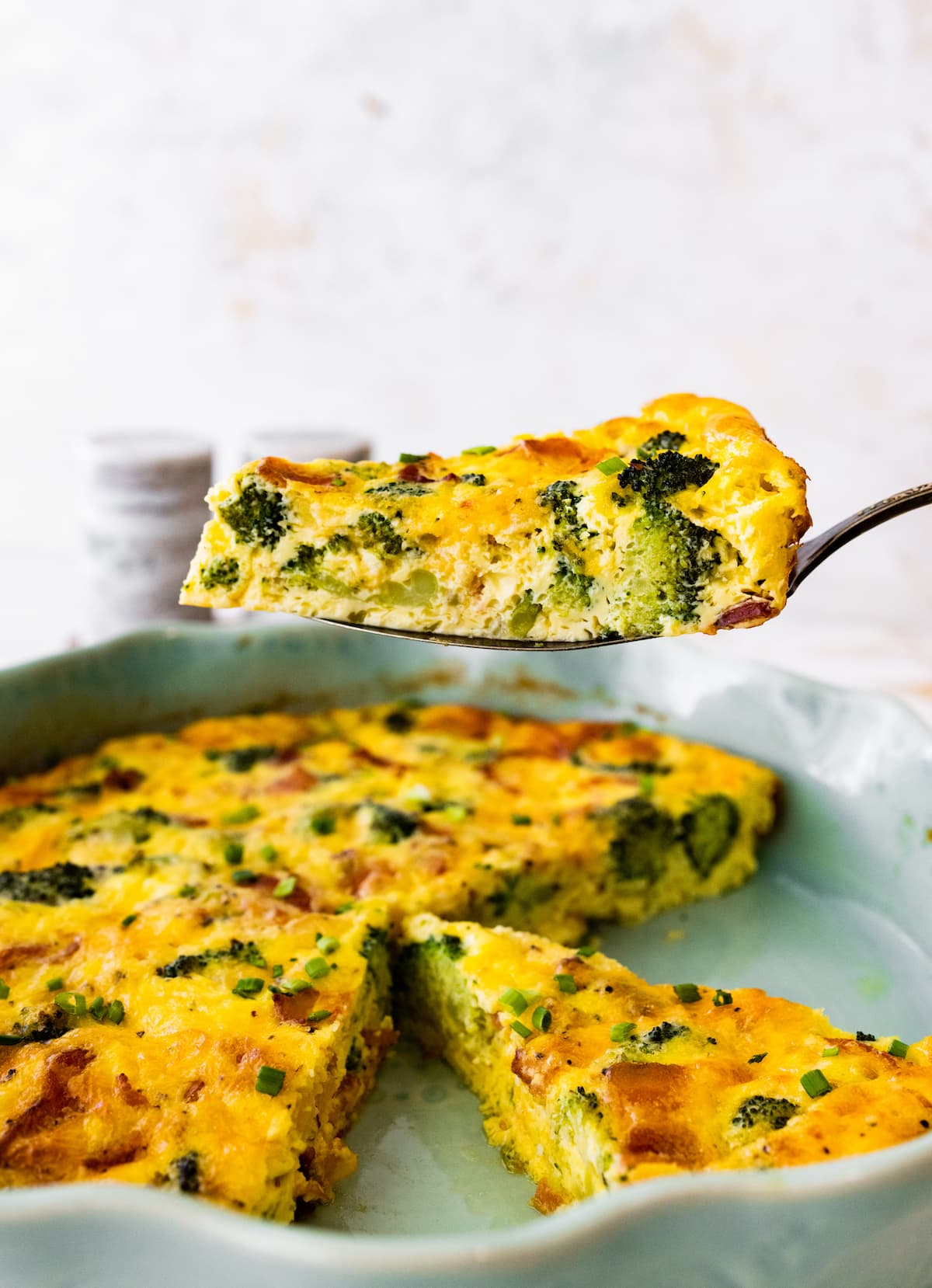 crustless quiche with broccoli, cheese, and bacon being lifted out of pie pan. 