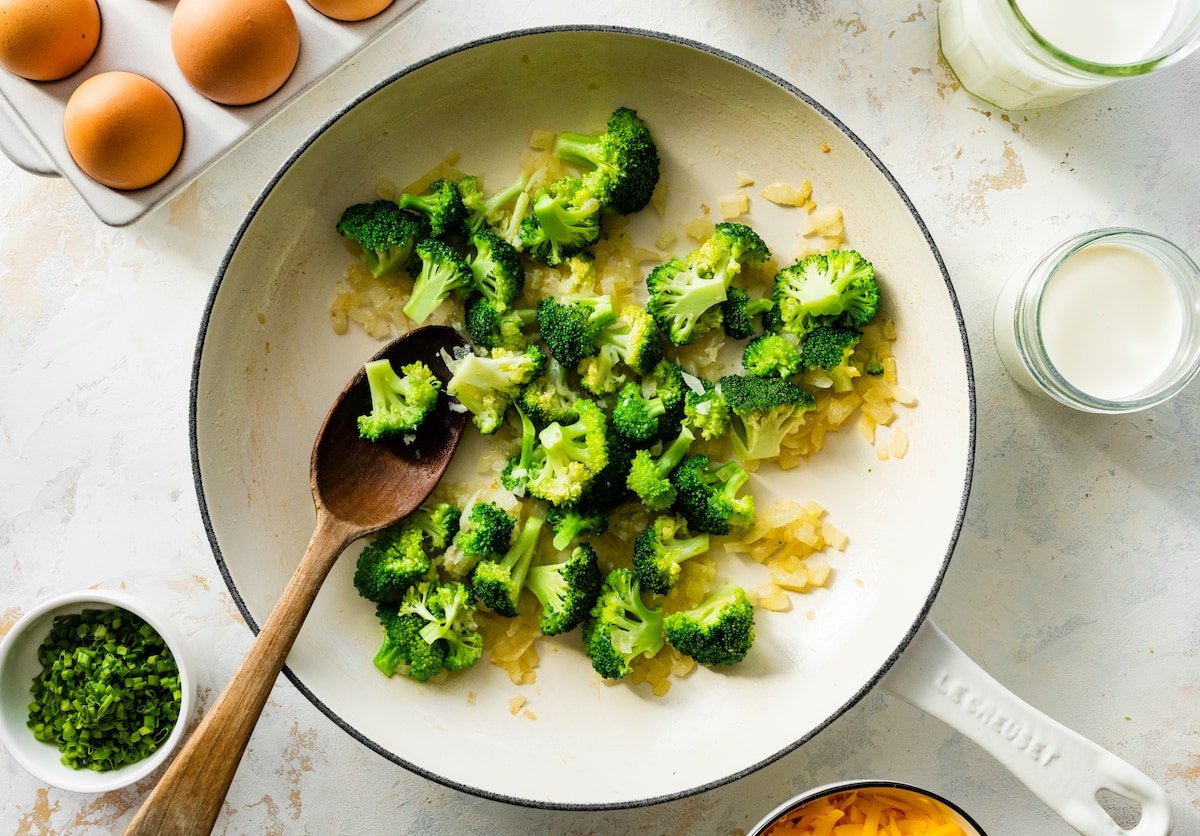 onion and broccoli cooking in skillet with wooden spoon. 