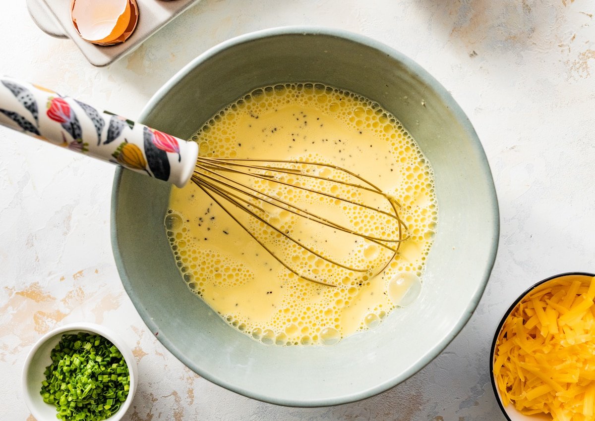 eggs, milk, and heavy cream being whisked together in bowl to make crustless quiche. 