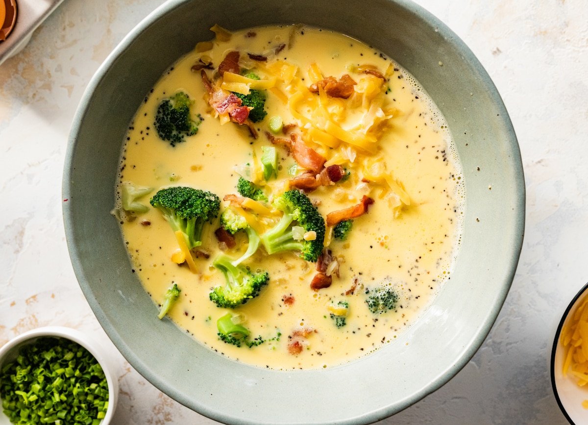 broccoli, bacon, and cheddar cheese being stirred into egg mixture to make crustless quiche. 