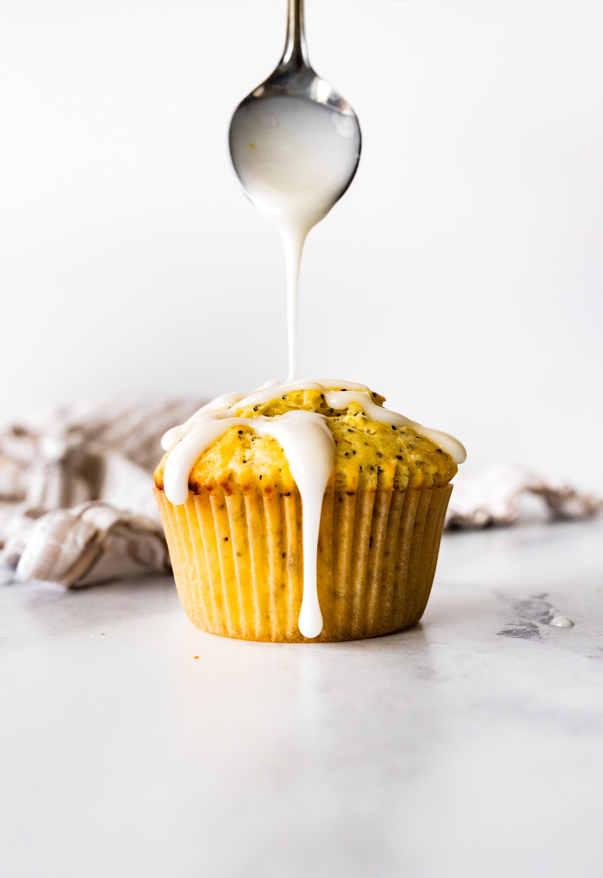 lemon glaze being drizzled over lemon poppy seed muffin. 