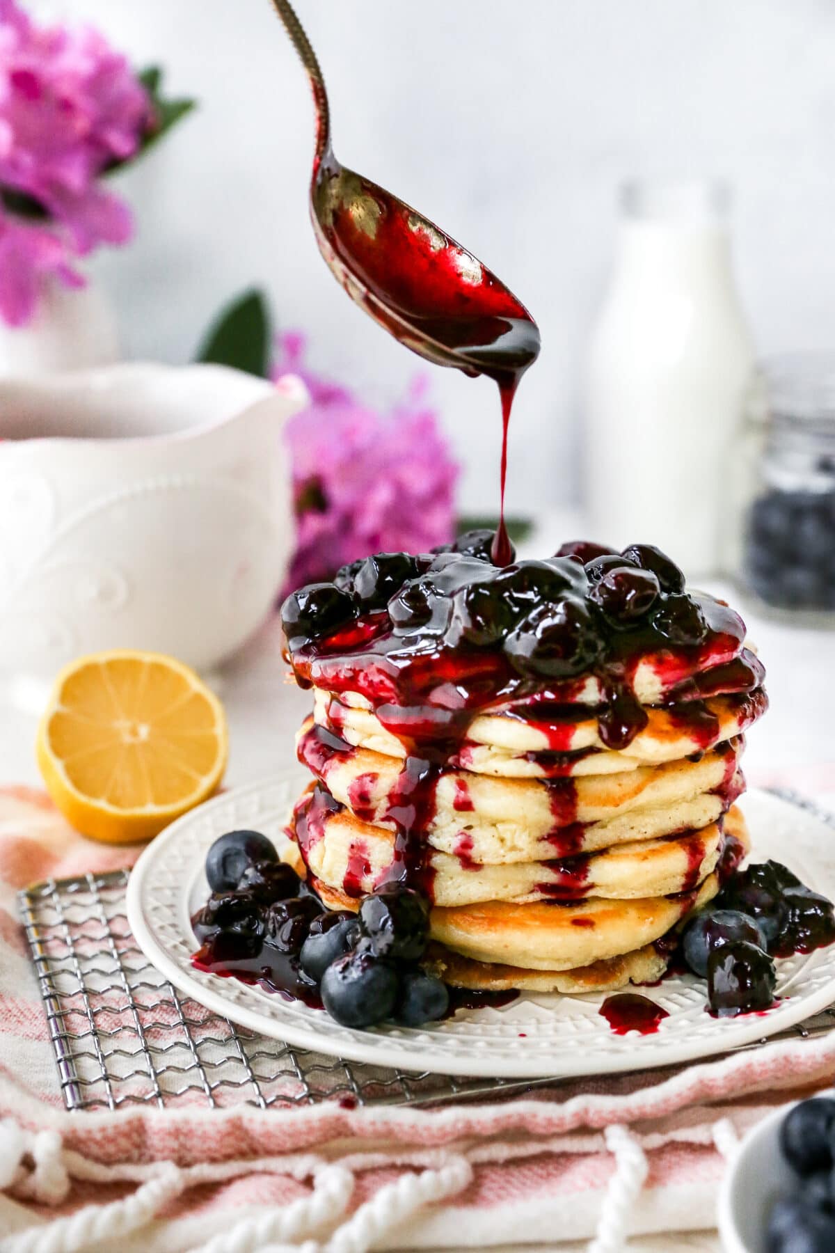 blueberry sauce being poured over stack of lemon ricotta pancakes. 