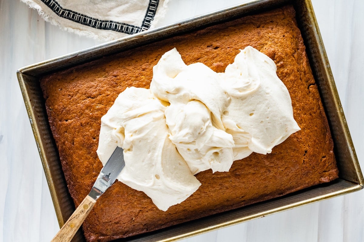 banana cake in pan with cream cheese frosting being spread on top. 