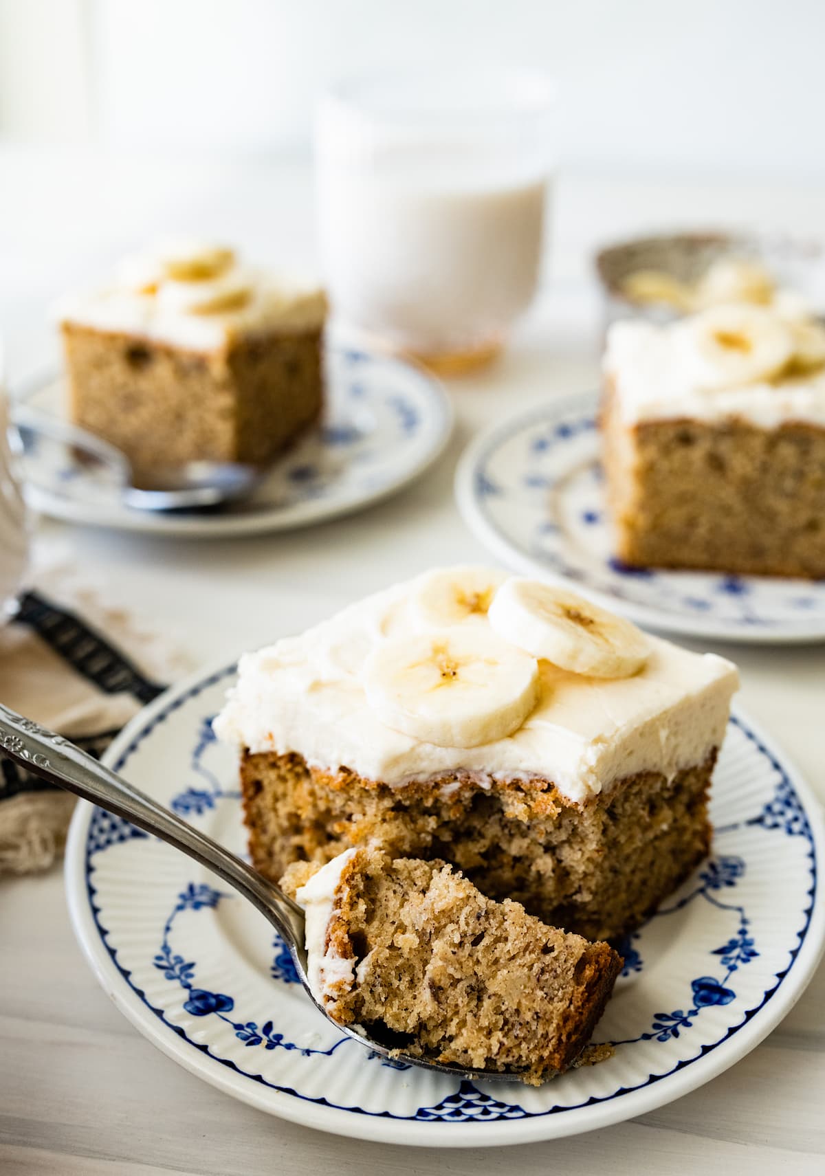 piece of banana cake with cream cheese frosting on plate with bite on fork. 