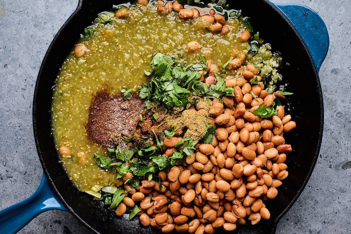 beans, salsa verde, cilantro, and spices cooking in cast iron skillet. 