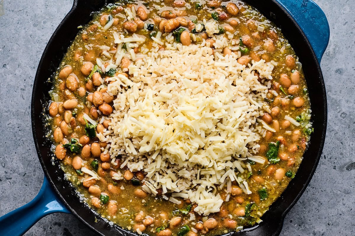 beans, rice, and salsa verde mixture cooking in cast iron skillet. 