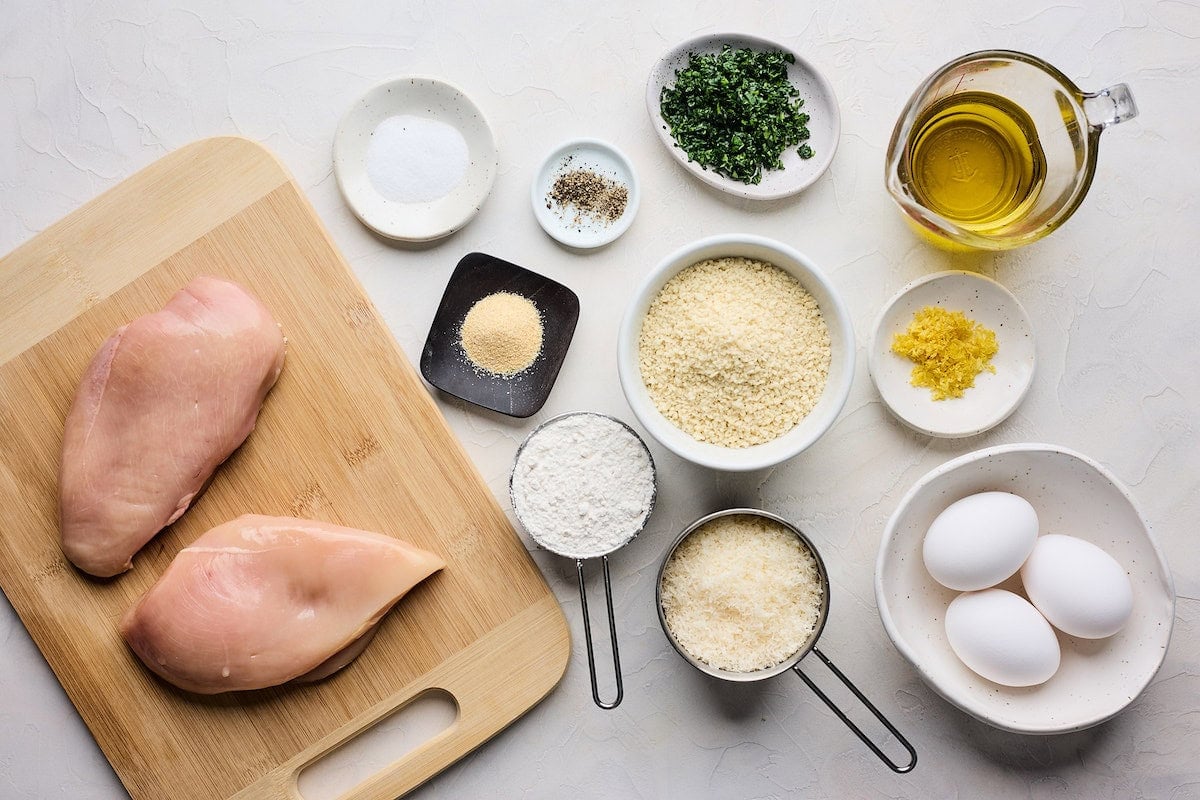 chicken breasts on cutting board and ingredients in bowls to make Chicken Milanese. 