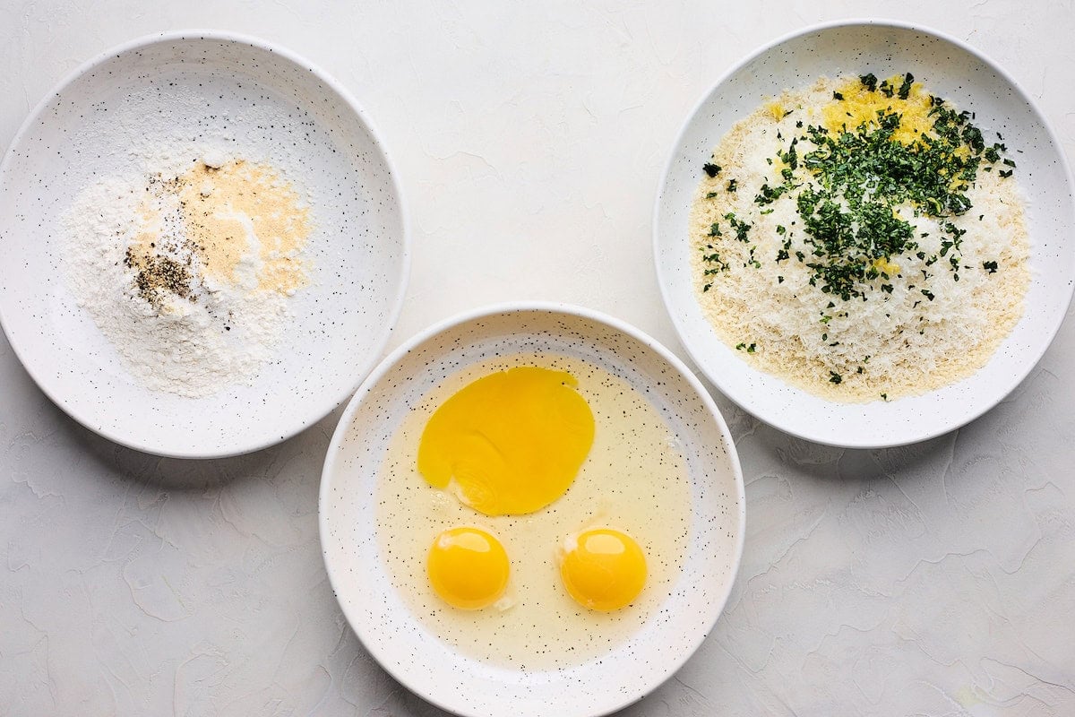 flour and spices in a bowl, eggs in a bowl, and panko bread crumbs and herbs in a bowl to make chicken Milanese. 