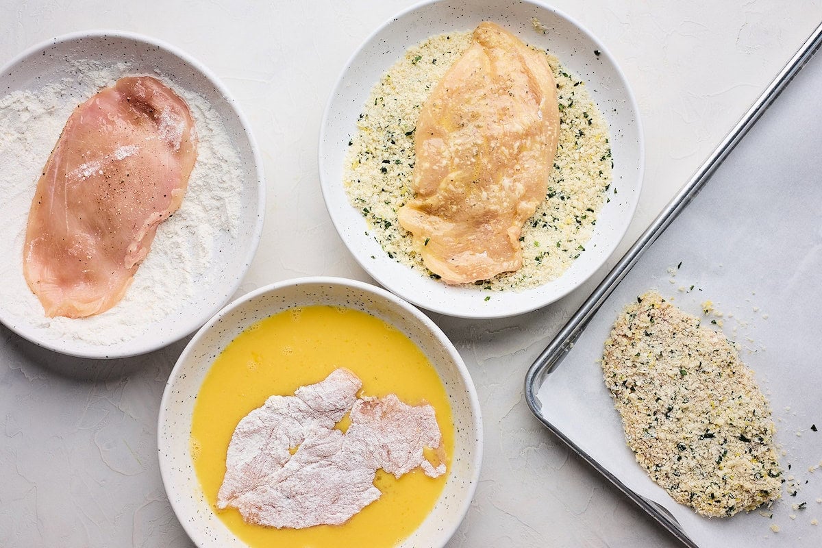 chicken breasts being dipped in flour, eggs, and bread crumbs to make chicken Milanese. 