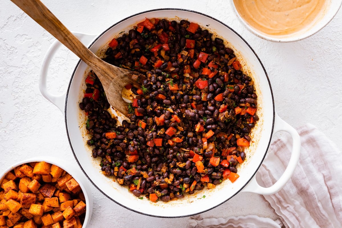 black beans with red peppers and spices in pot with wooden spoon. 