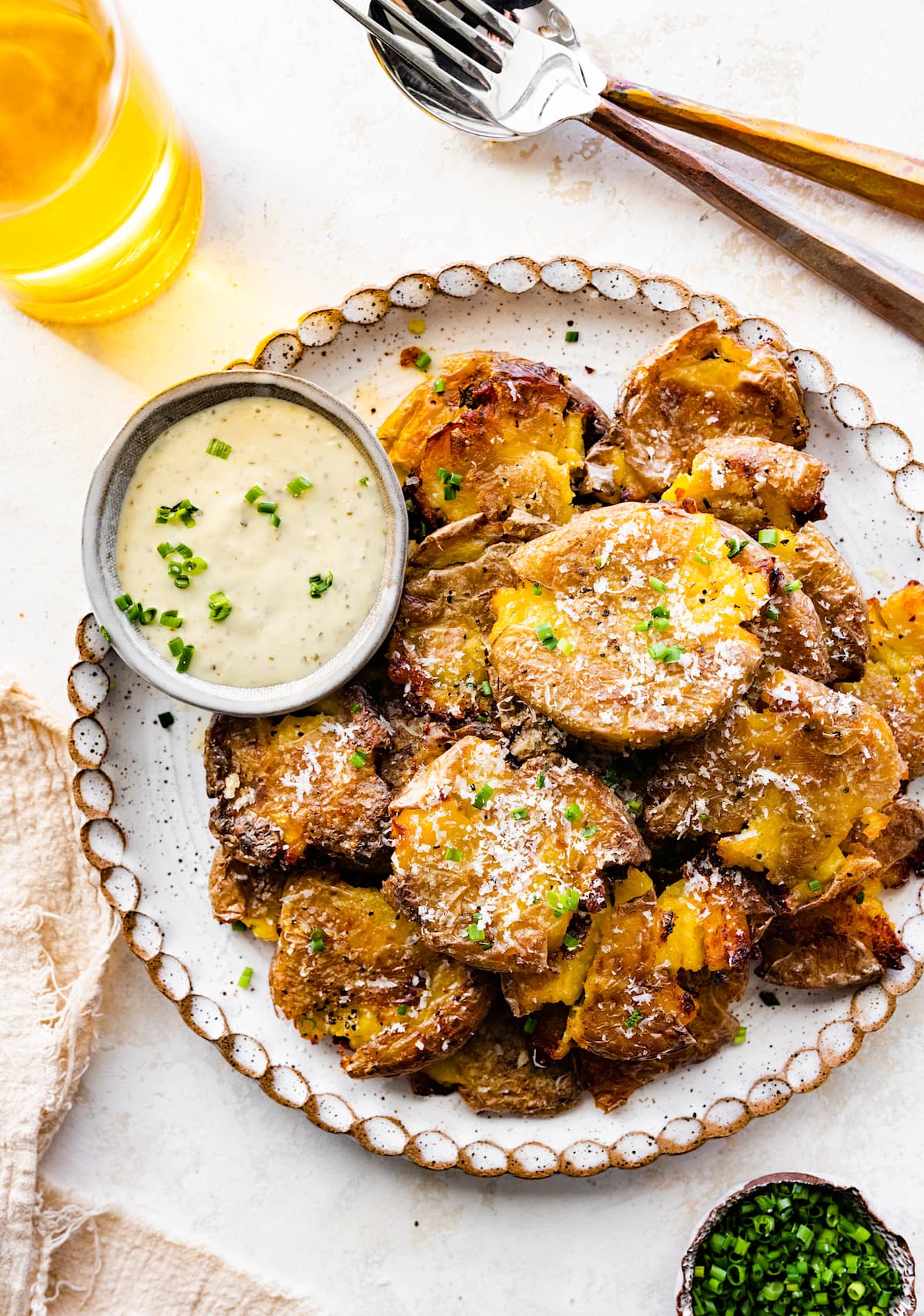 crispy smashed potatoes on plate with parmesan cheese, chives, and dipping sauce. 