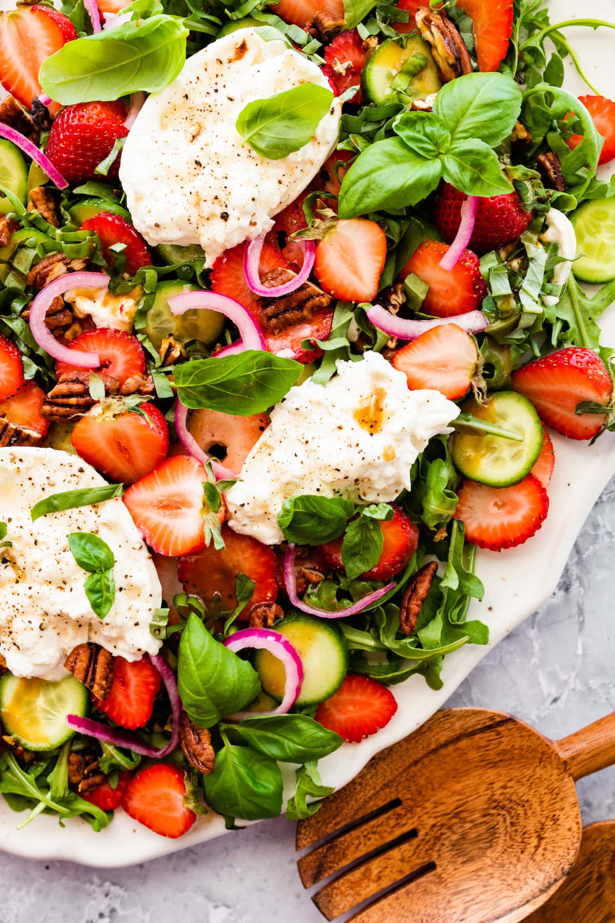 strawberry burrata salad on platter with wood salad servers. 