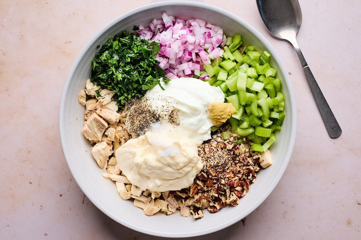 chicken salad ingredients in white mixing bowl with spoon. 