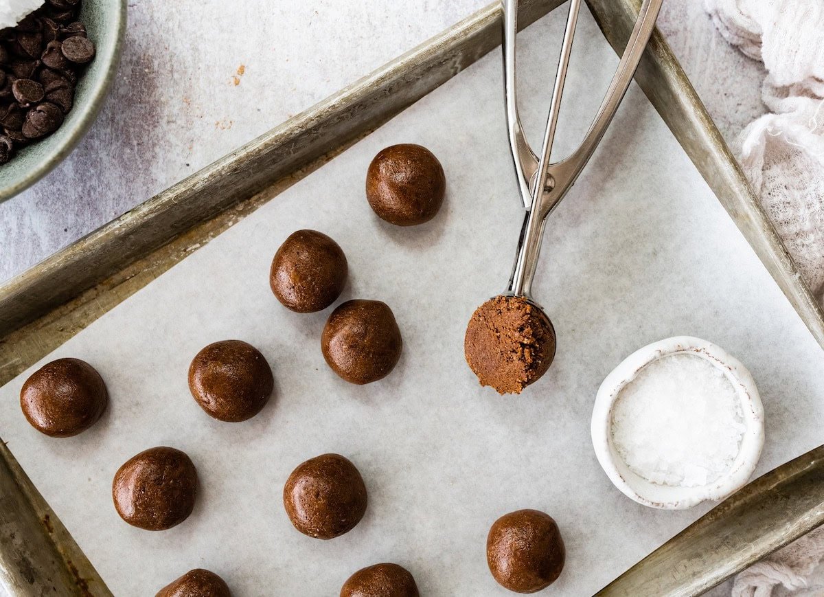 brownie protein balls being scooped onto baking sheet with parchment paper. 