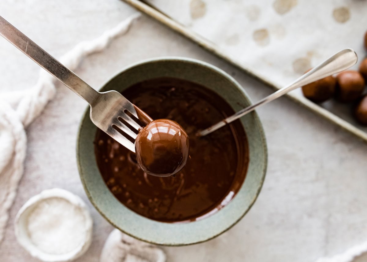 brownie protein ball being dipped in melted chocolate with fork. 