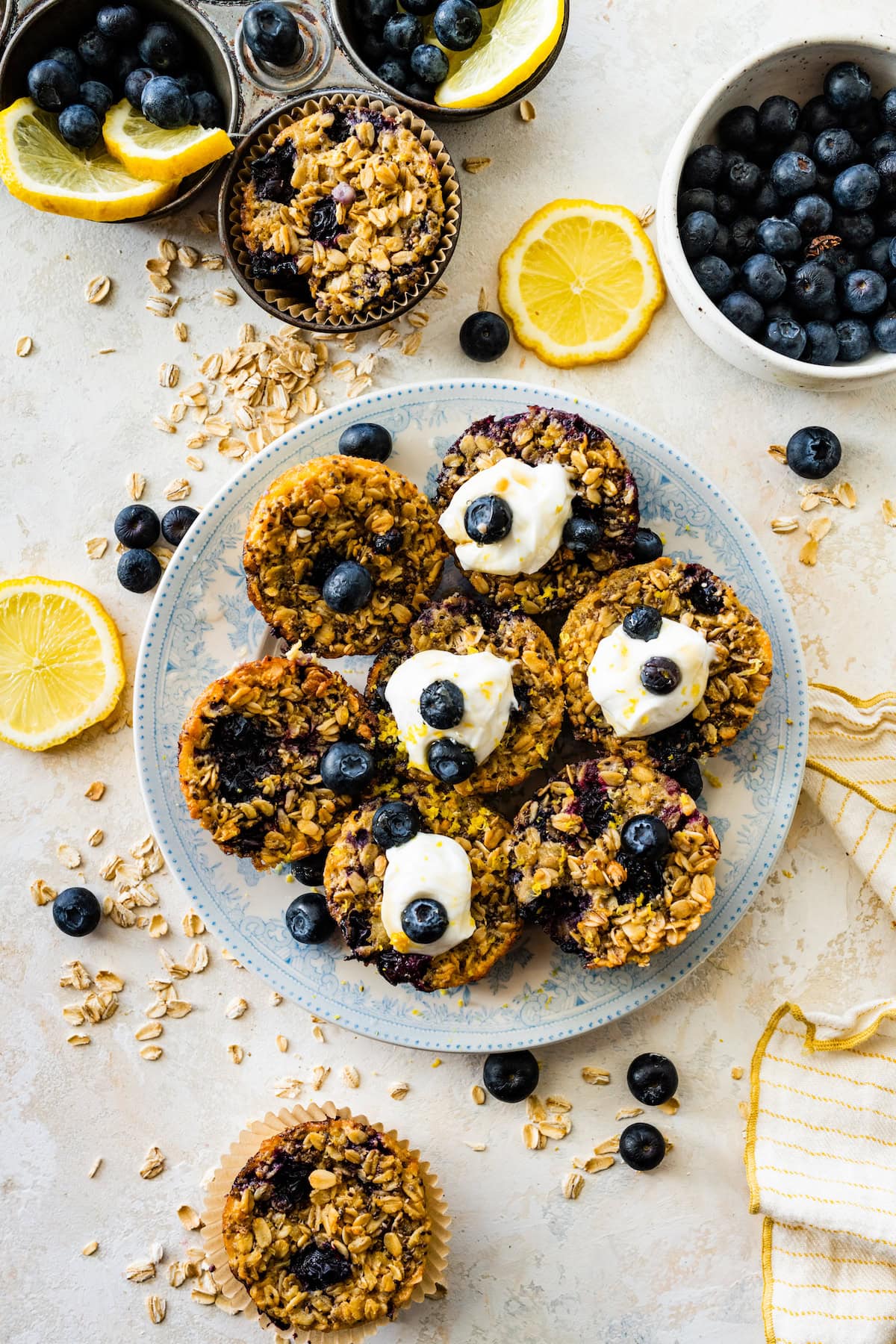 lemon blueberry baked oatmeal cups on plate with greek yogurt, lemons, and fresh blueberries. 