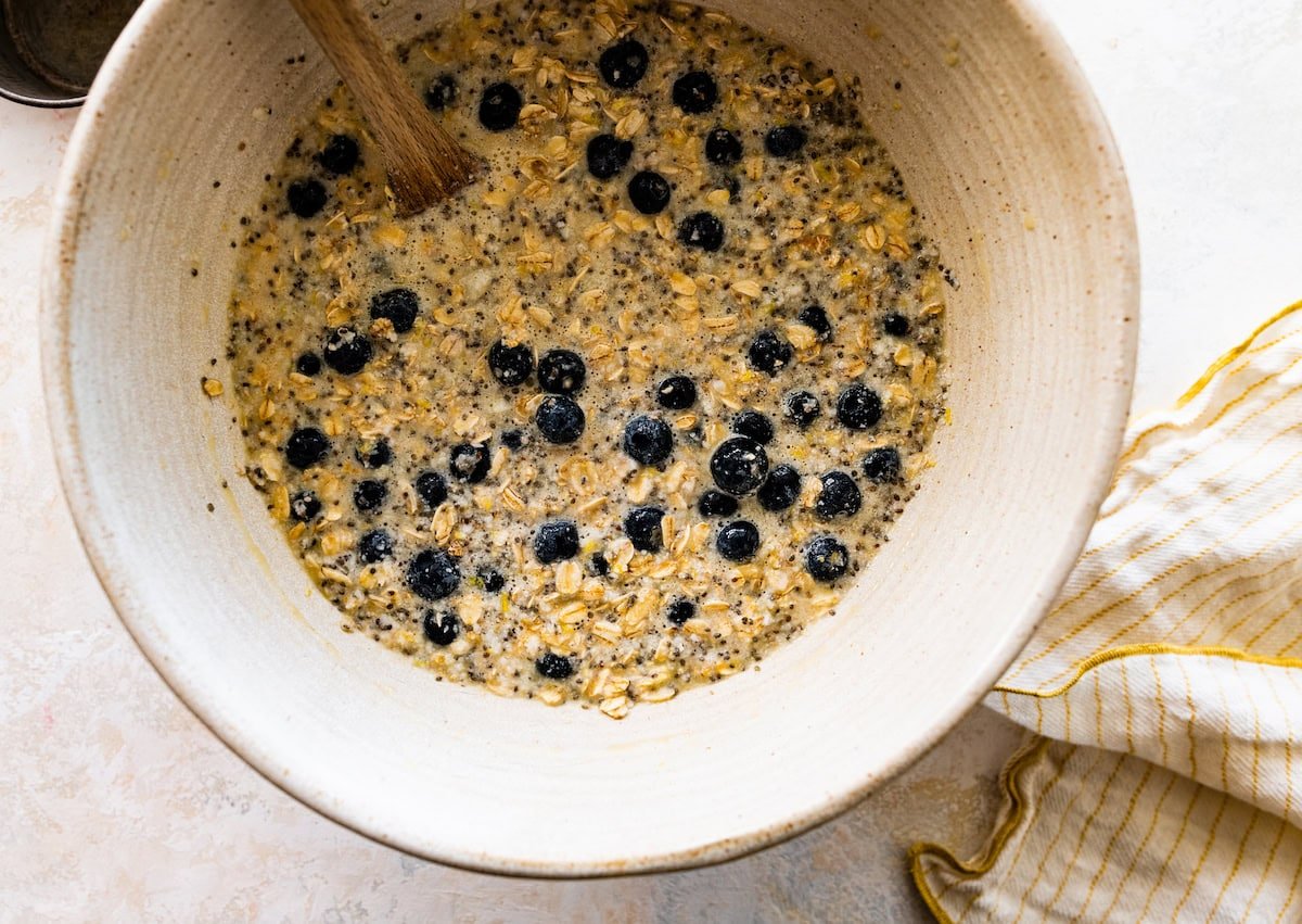 blueberries being stirred into baked oatmeal mixture in mixing bowl with wooden spoon. 