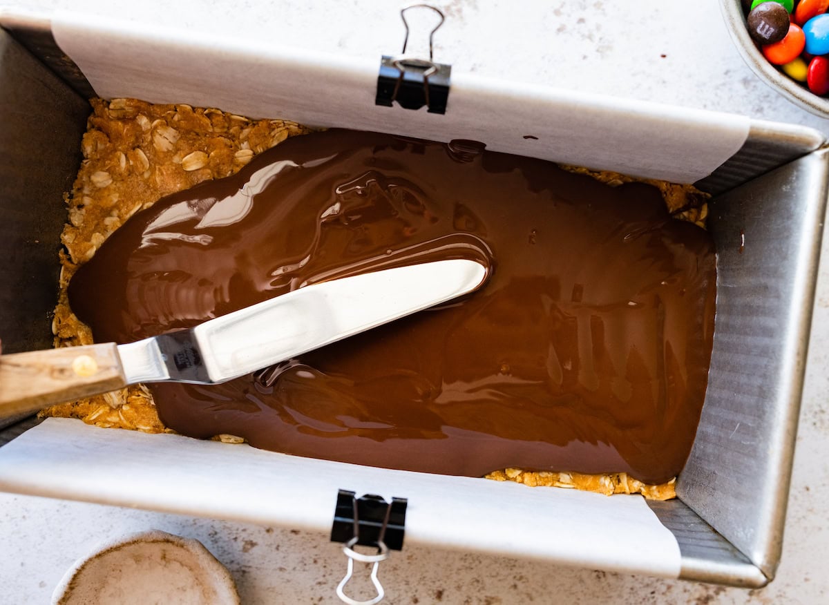melted chocolate being spread over no bake monster cookie bars. 