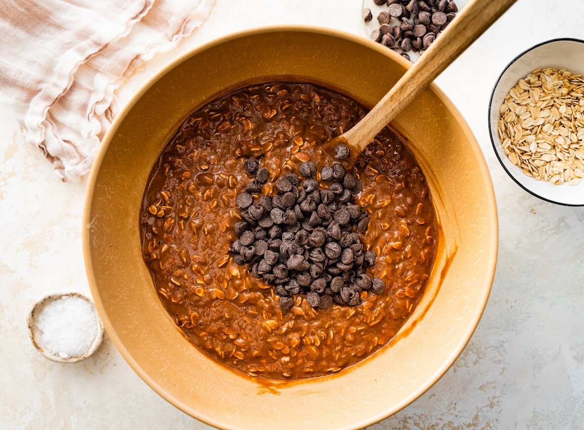 chocolate peanut butter baked oatmeal mixture in mixing bowl with chocolate chips in mixing bowl with spatula.