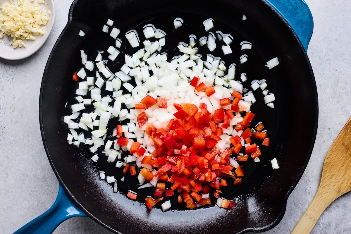 onion and red bell peppers cooking in cast iron skillet.