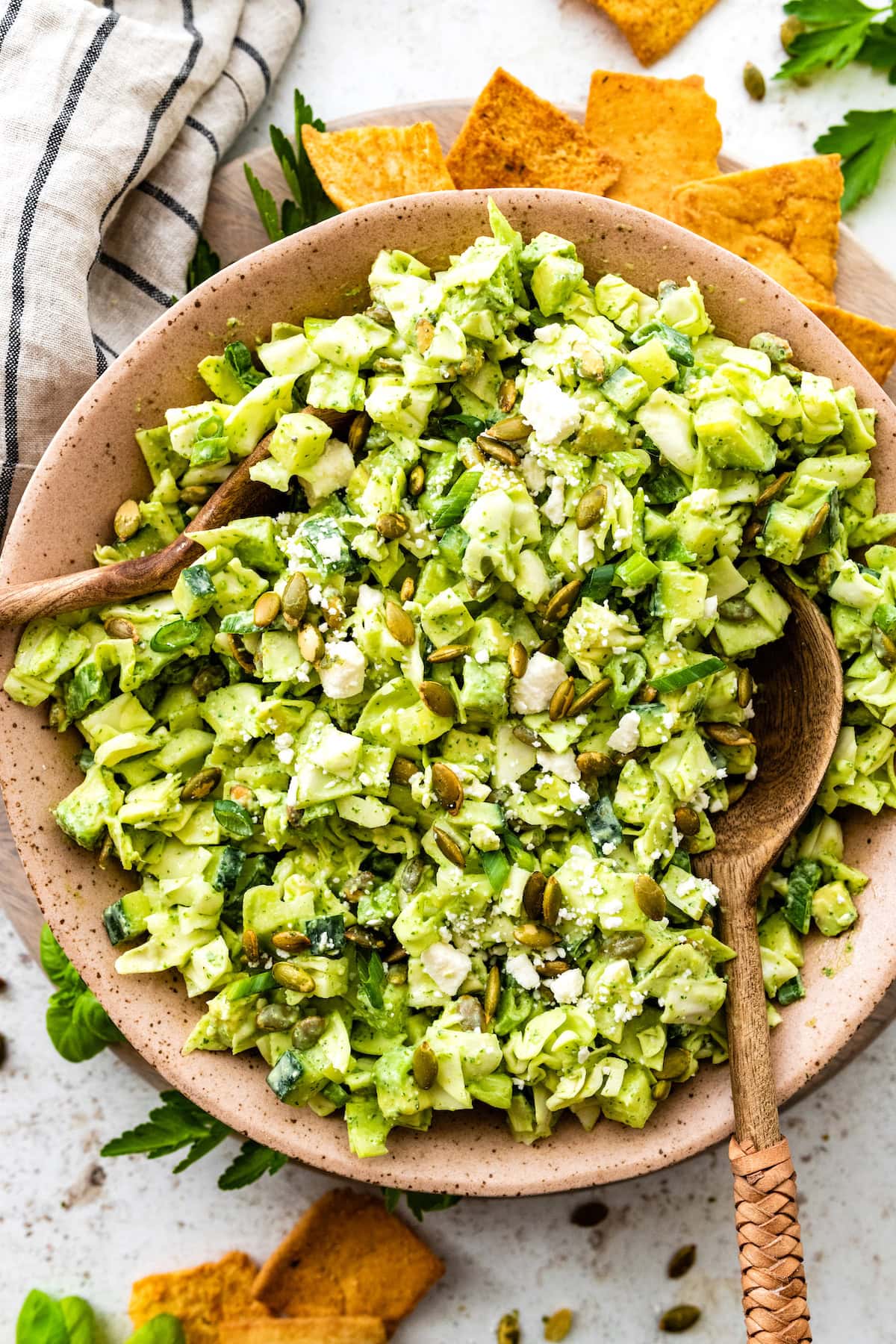 green goddess salad in serving bowl with wood salad servers and chips on the side.
