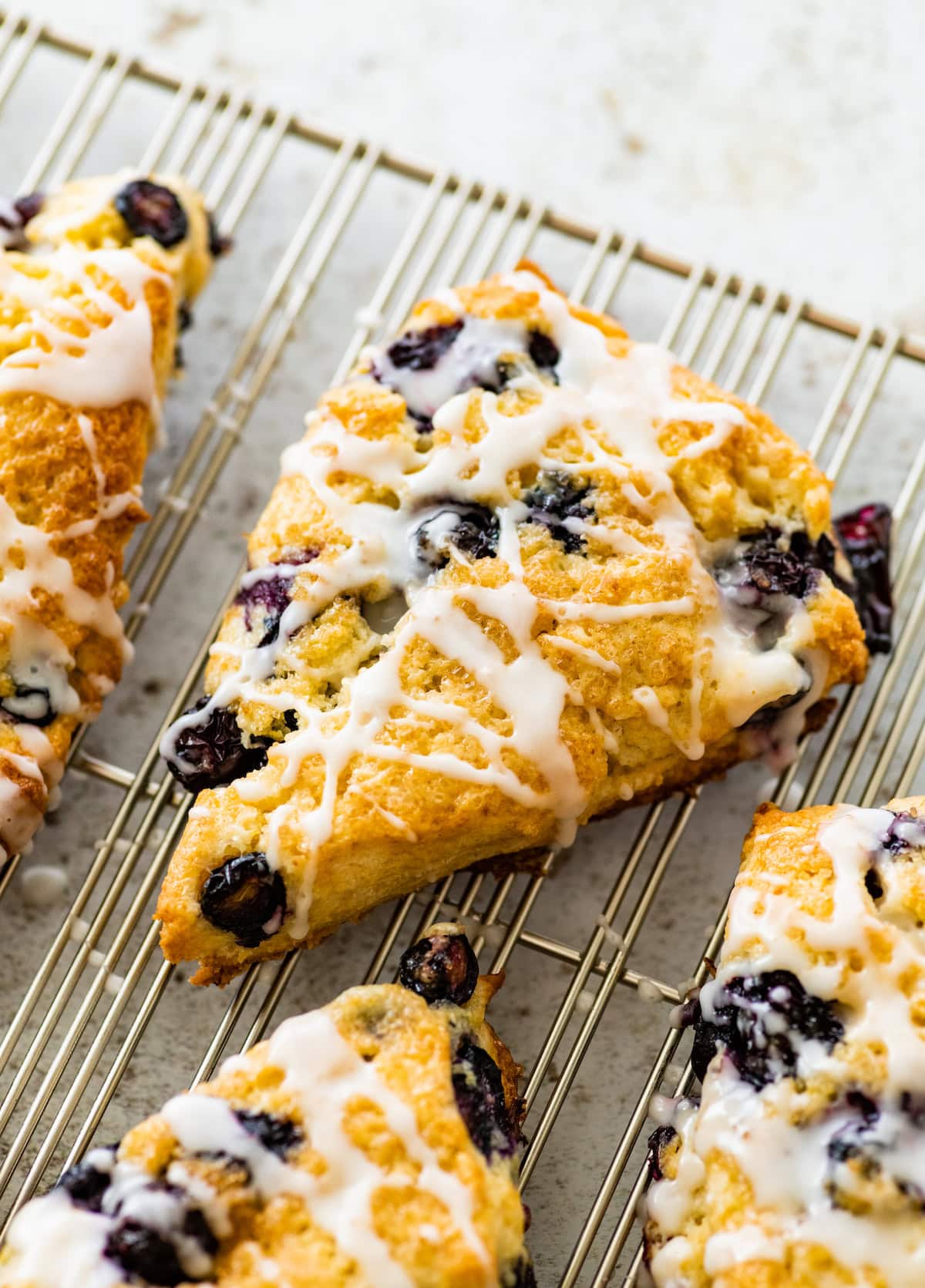 lemon blueberry scone with lemon glaze on cooling rack. 