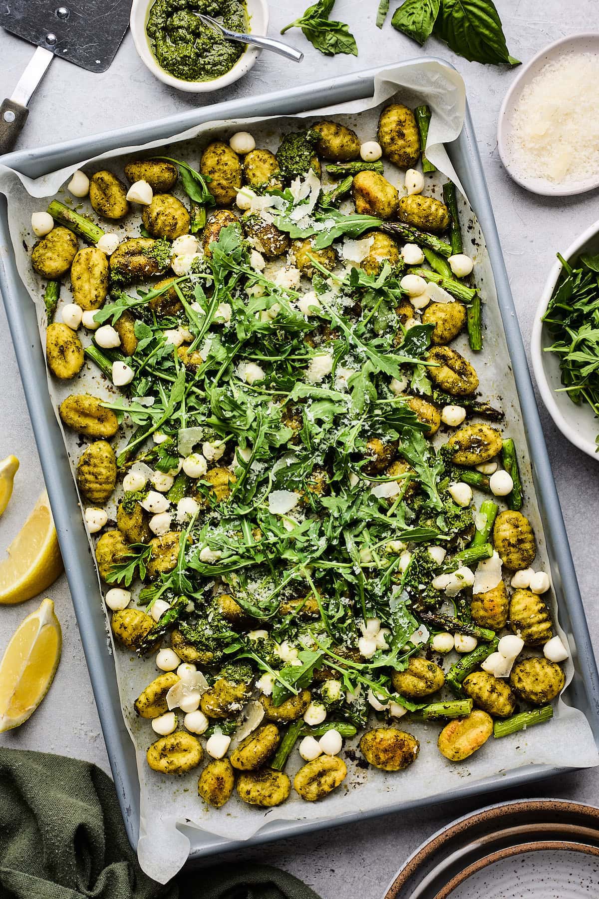 spring sheet pan gnocchi with pesto, fresh mozzarella, arugula, and Parmesan cheese on sheet pan.