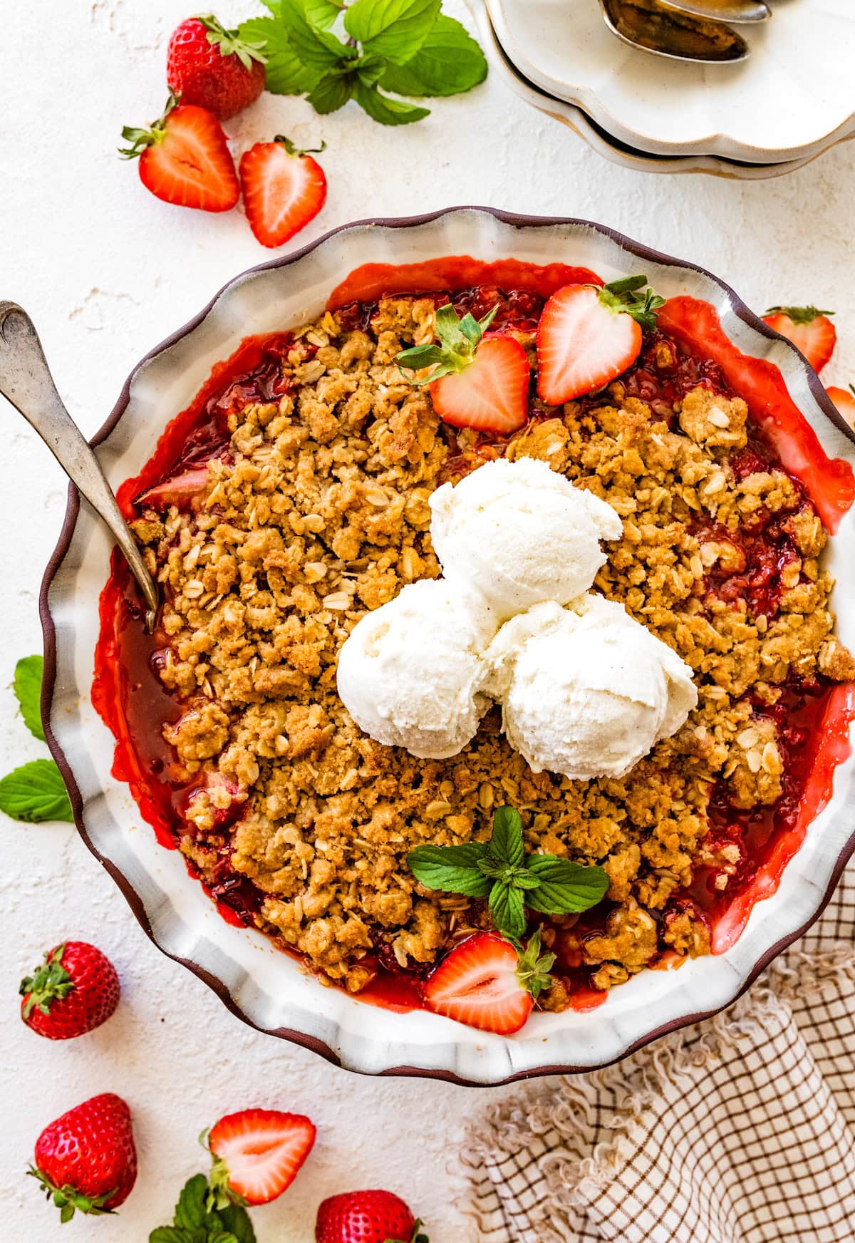 strawberry crisp in baking dish with three scoops of vanilla ice cream.