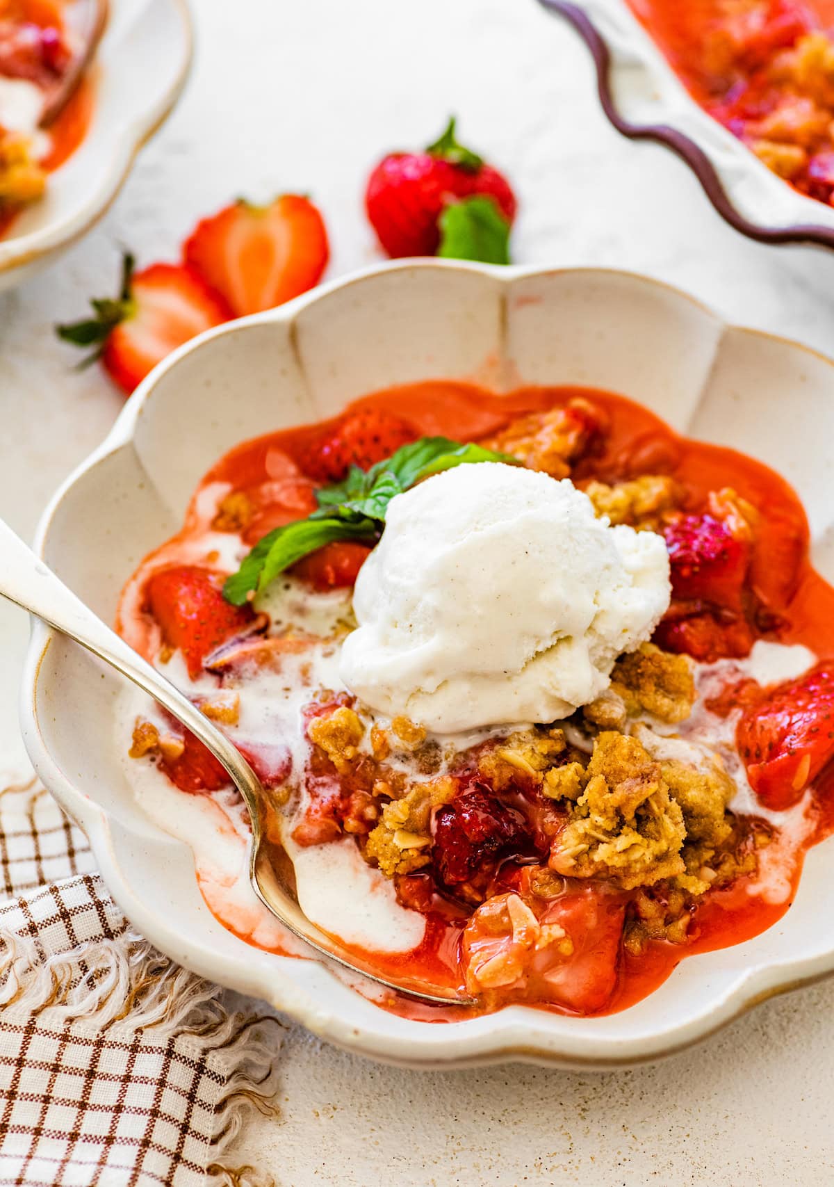 strawberry crisp with a scoop of vanilla ice cream in bowl with spoon.