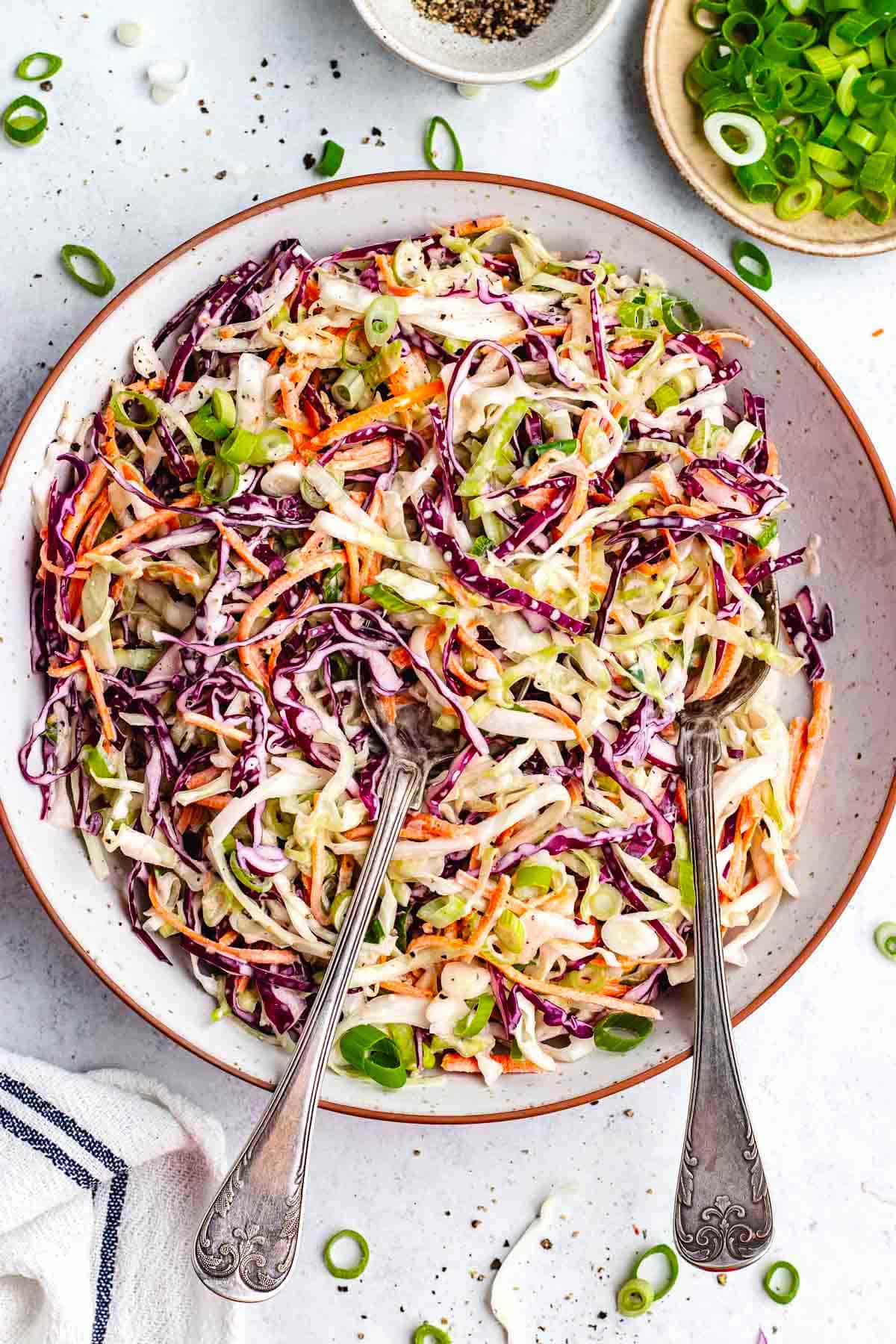 creamy coleslaw in bowl with serving spoons.