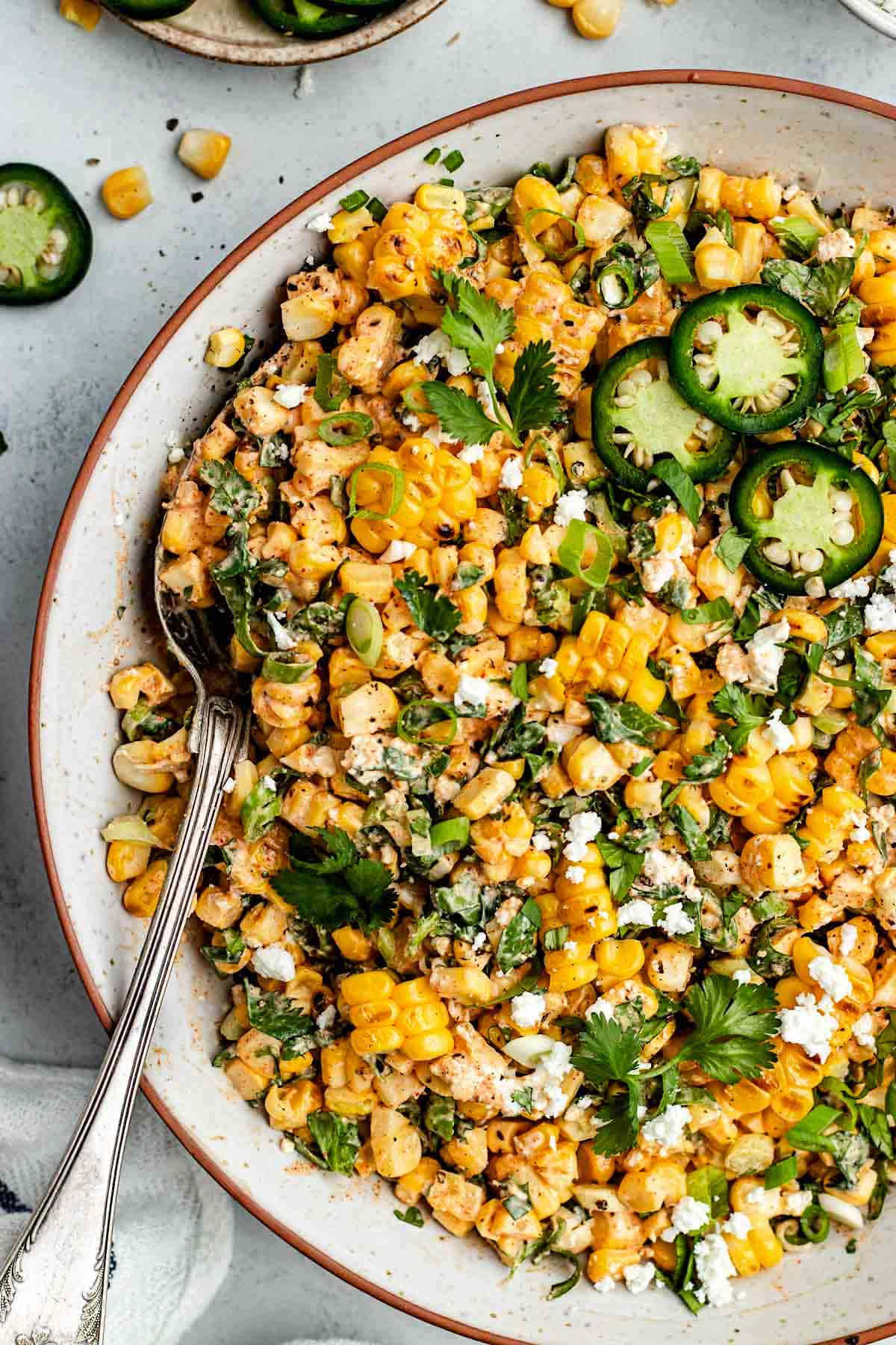 close up of Mexican corn salad in bowl with serving spoon.