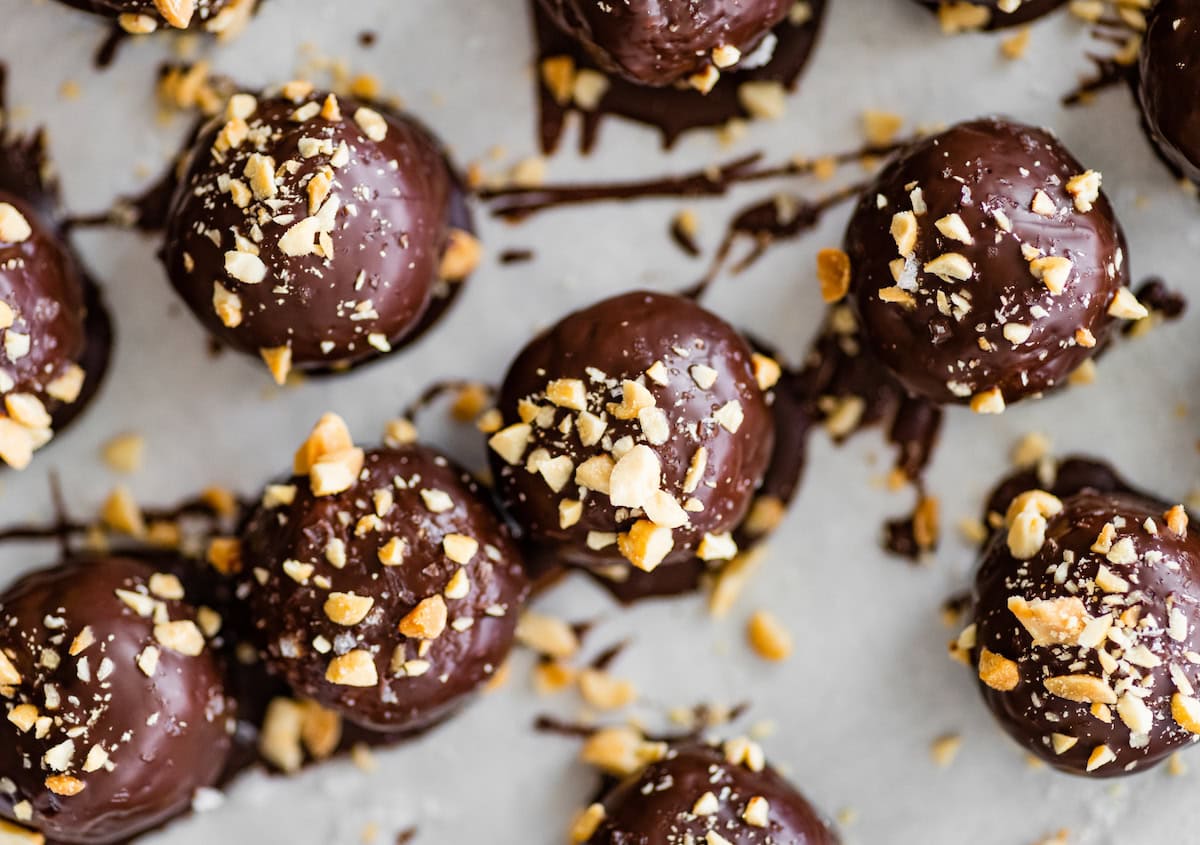 close up of snickers protein balls topped with chopped peanuts on parchment paper.