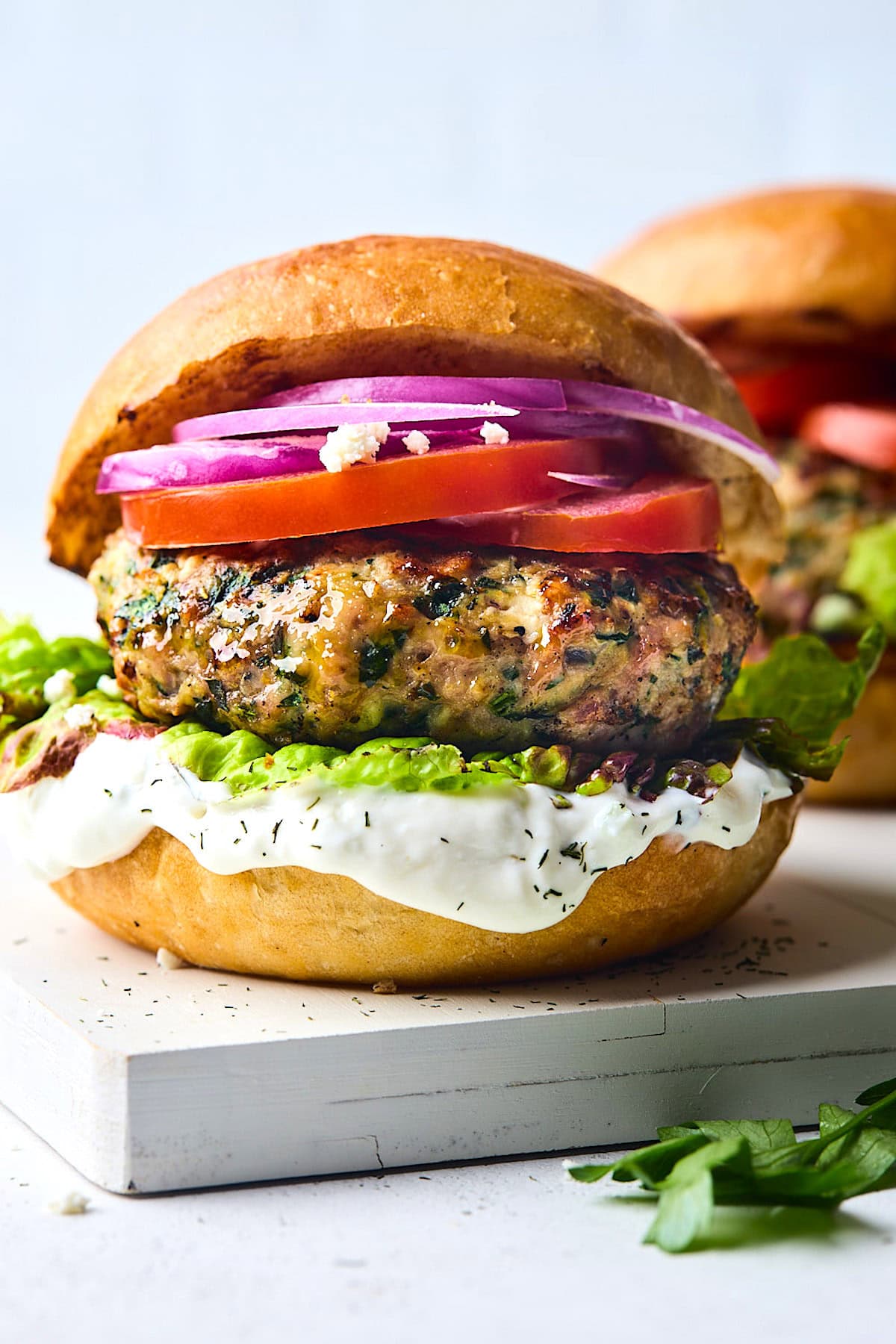 close up of Greek turkey burger on bun with red onion, tomato, lettuce, and tzatziki sauce.