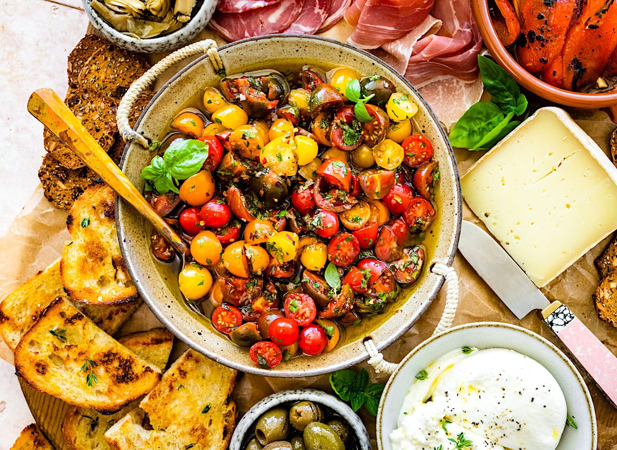 marinated tomatoes in bowl with spoon on charcuterie board.