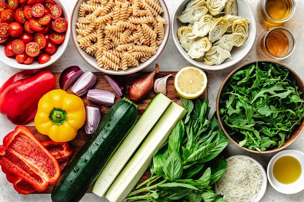 ingredients in bowls and vegetables on wood cutting board to make grilled vegetable pasta salad. 