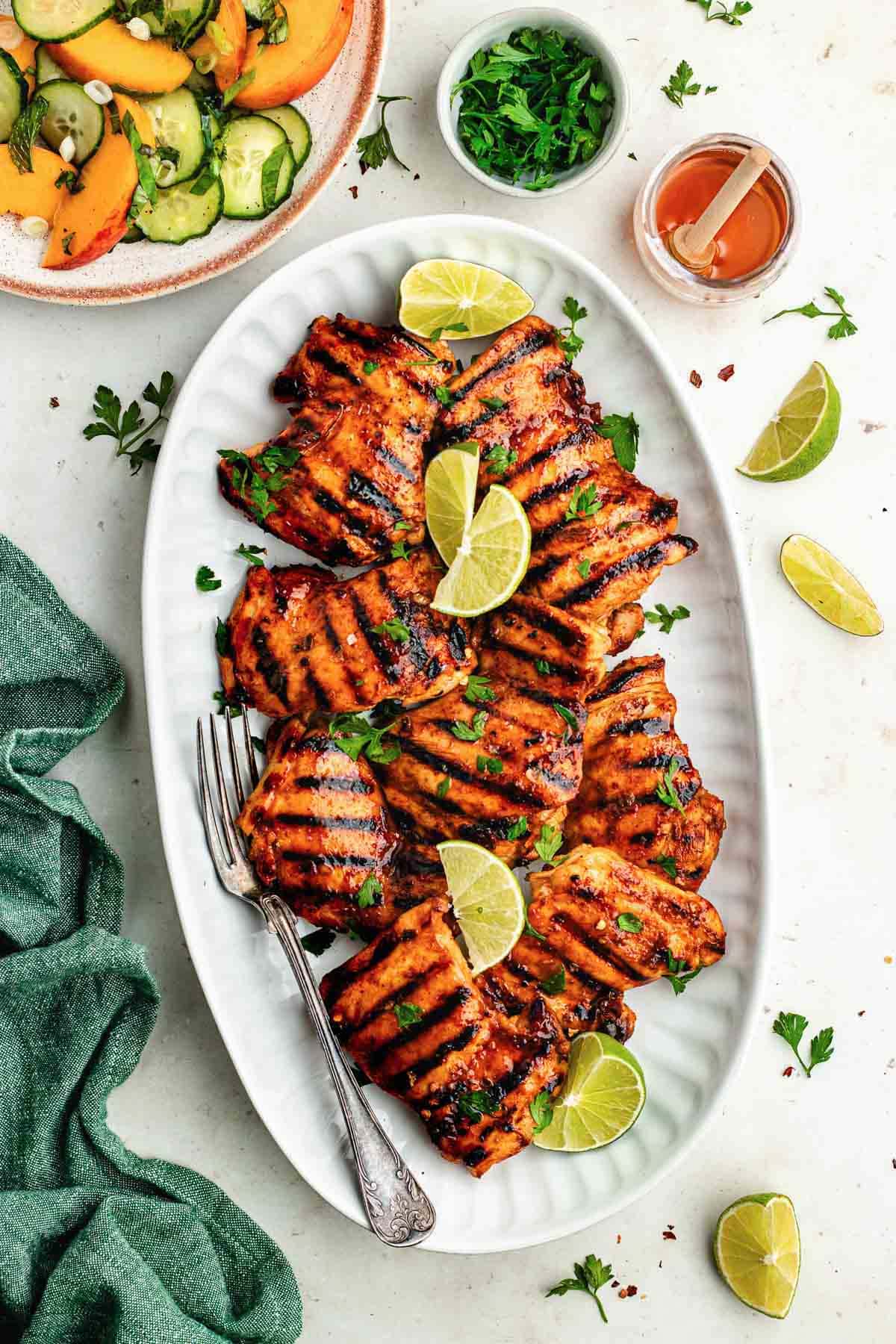 grilled honey lime chicken on platter with lime wedges and serving fork. 