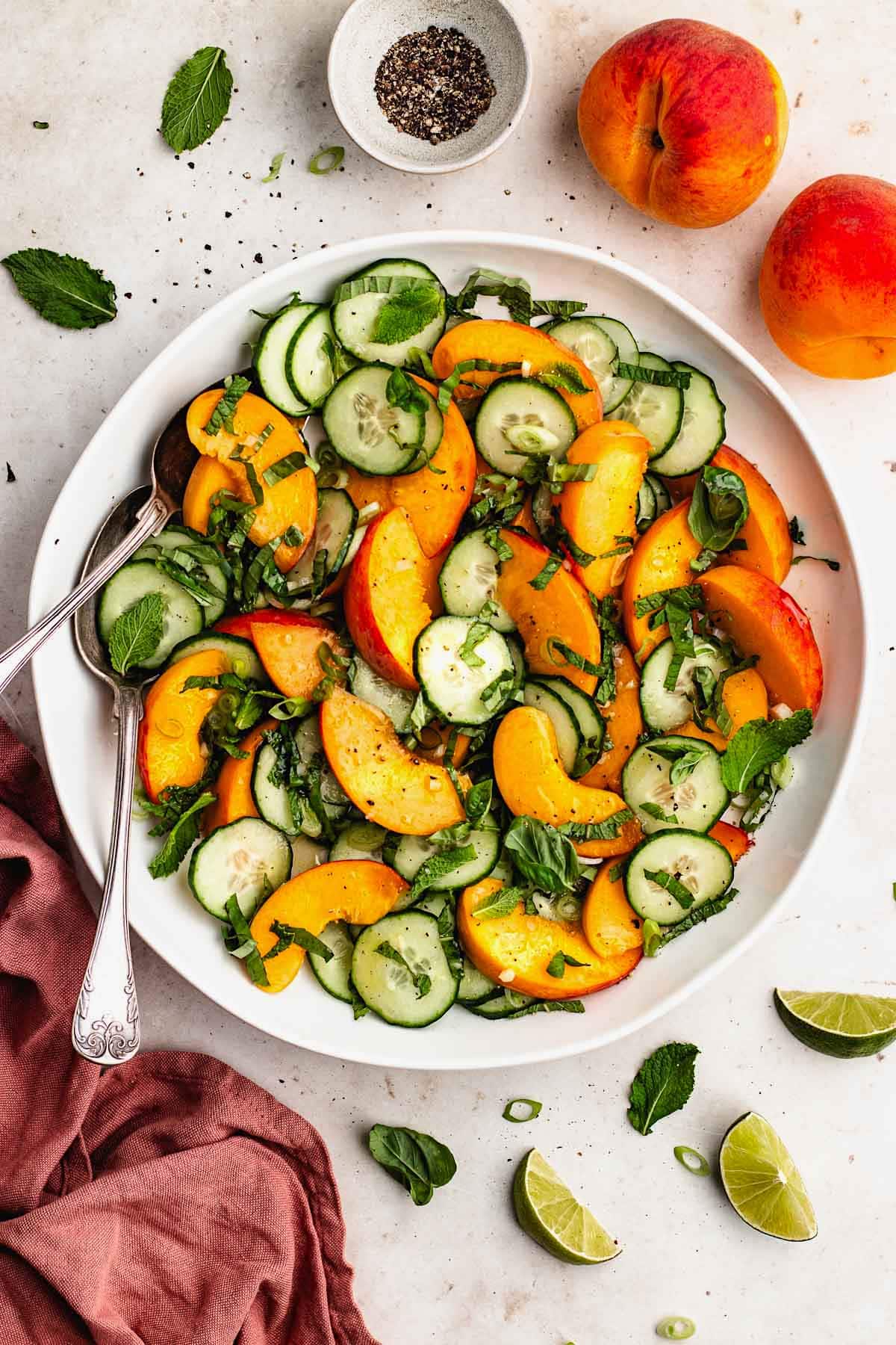 peach cucumber salad with fresh herbs in white serving bowl with serving spoons.